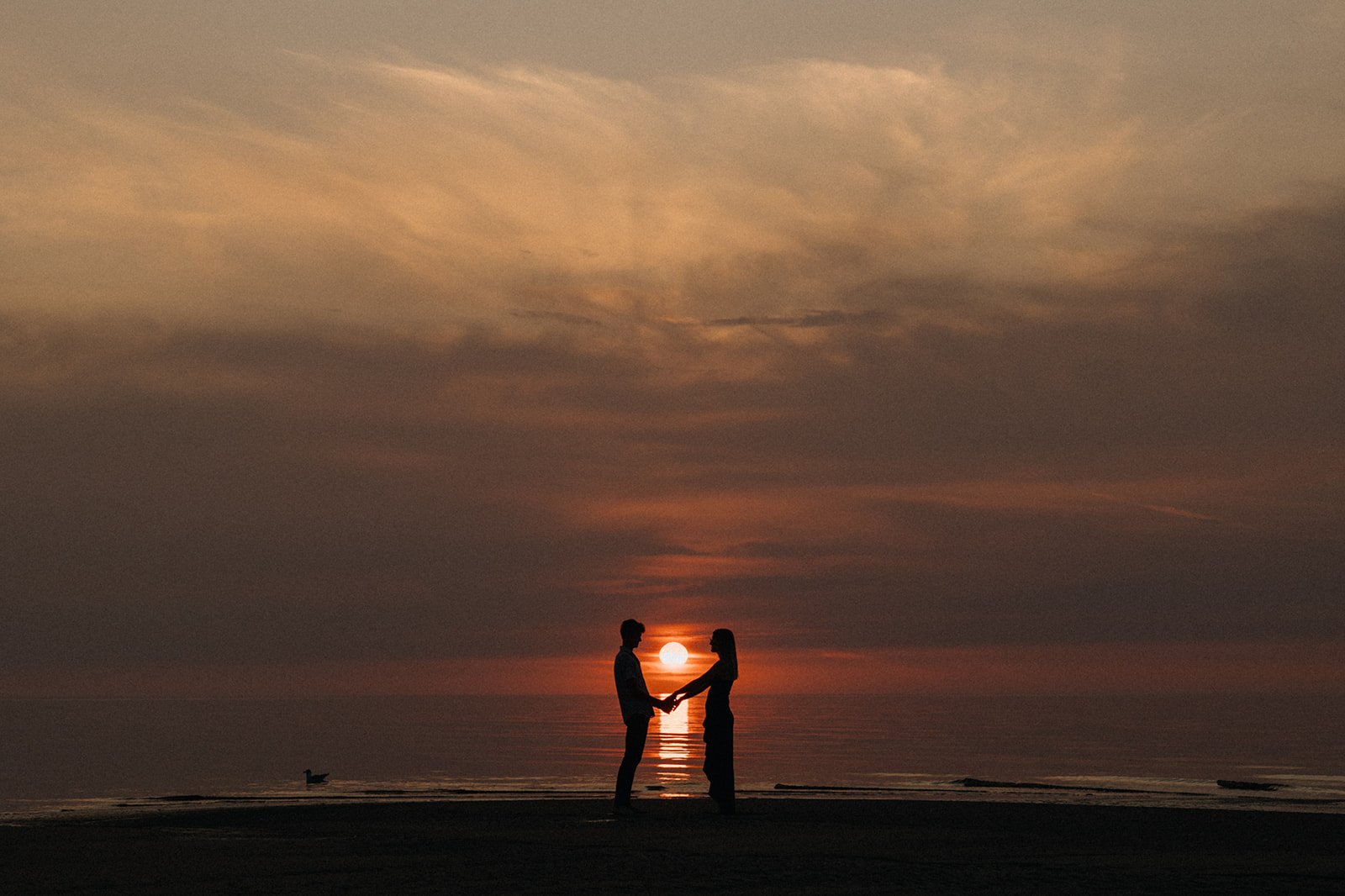 Silhouette of a couple holding hands at sunset on Grand Beach with the sun reflecting over Lake Winnipeg