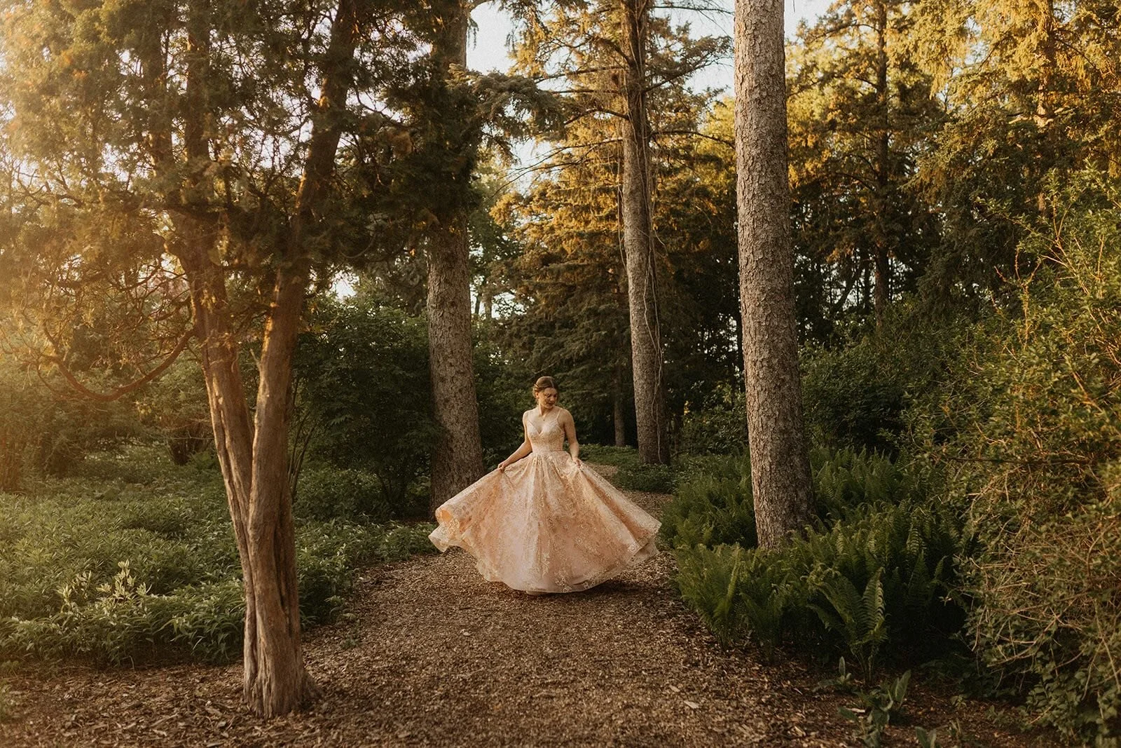 Grad portrait at Assiniboine Park English Garden in Winnipeg with a flowing dress on a tree-lined path