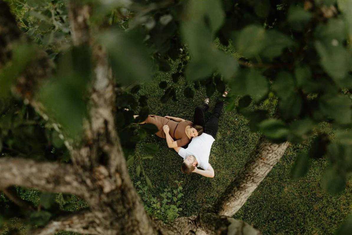 Couple lying together in the grass during a creative engagement session in Winnipeg photographed from above through trees