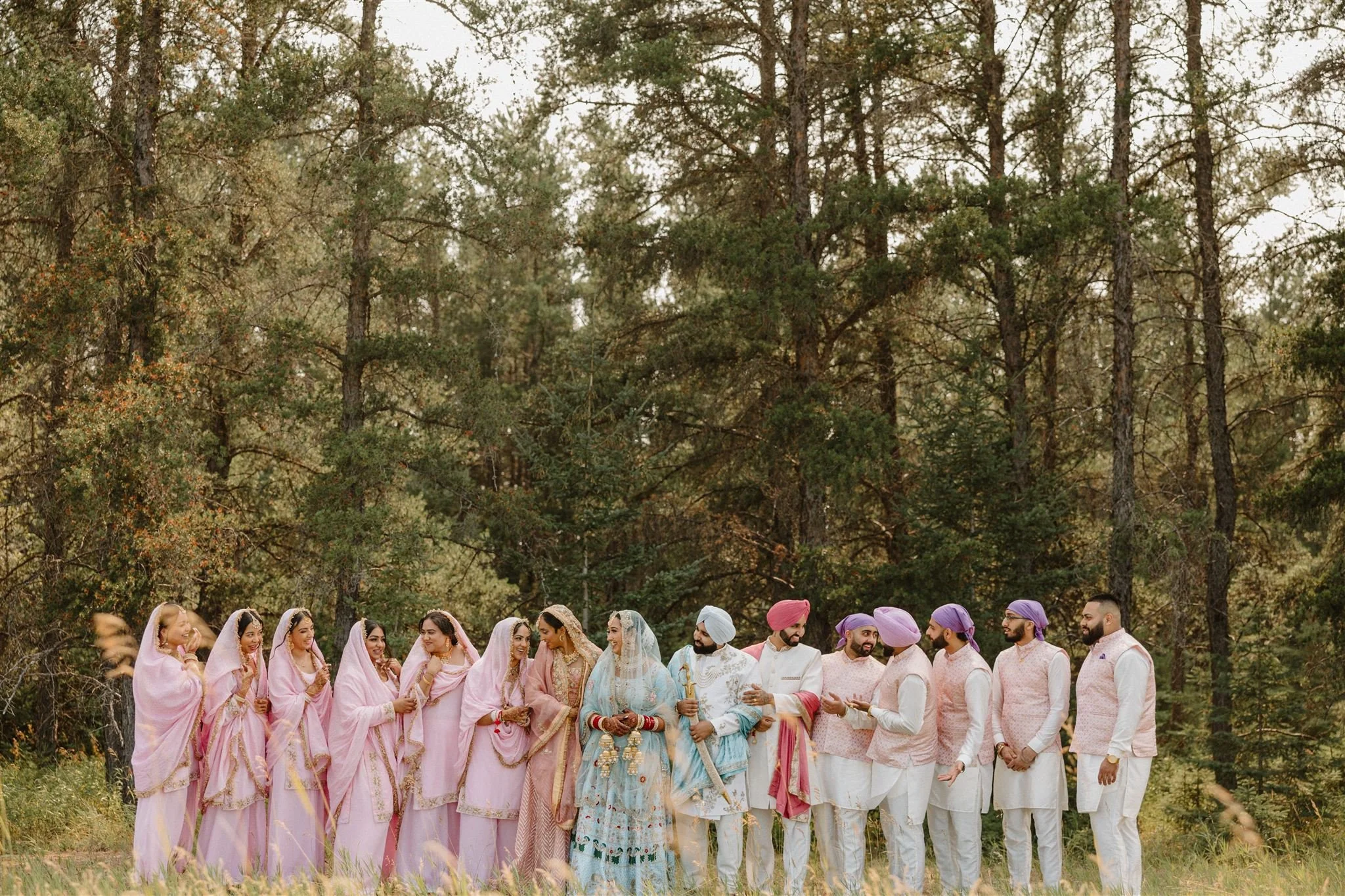 Wedding party gathered outdoors during a Sikh wedding in Winnipeg, with bridesmaids and groomsmen in coordinated traditional outfits surrounded by trees