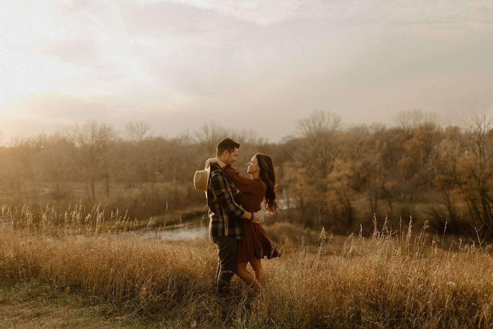 Couple embracing in a golden field at sunset in St Malo Park Manitoba with warm autumn tones and soft light