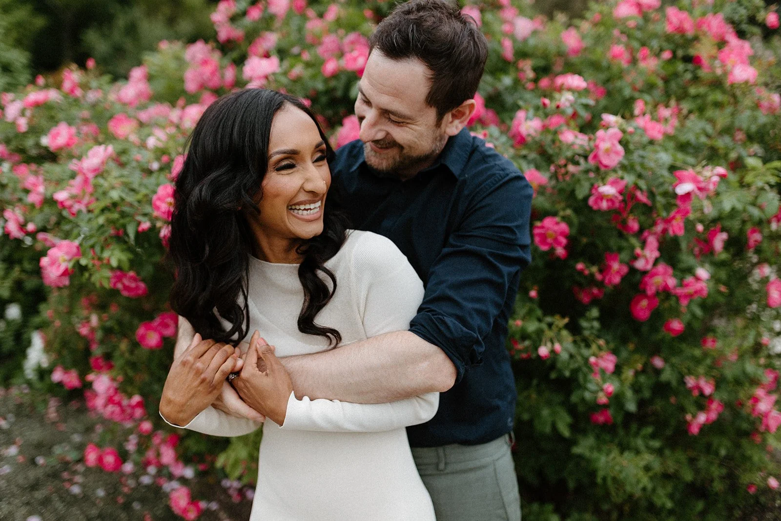 Couple embracing in front of blooming flowers during an engagement session at the English Garden in Assiniboine Park Winnipeg