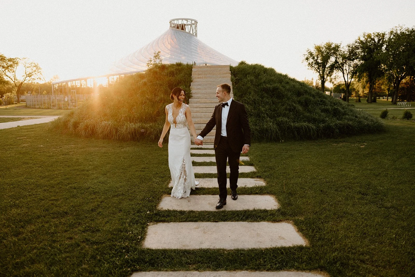 Wedding couple walking at sunset outside The Leaf Winnipeg, with warm light on the glass pavilion