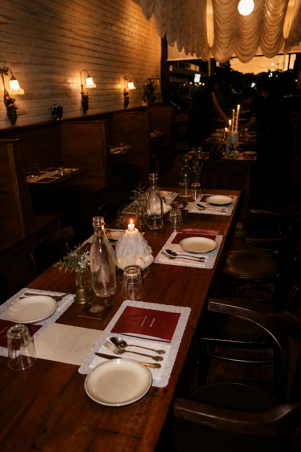 A beautifully set dining table in a dimly lit restaurant with candles, glass bottles, and plates ready for a meal, during the evening.