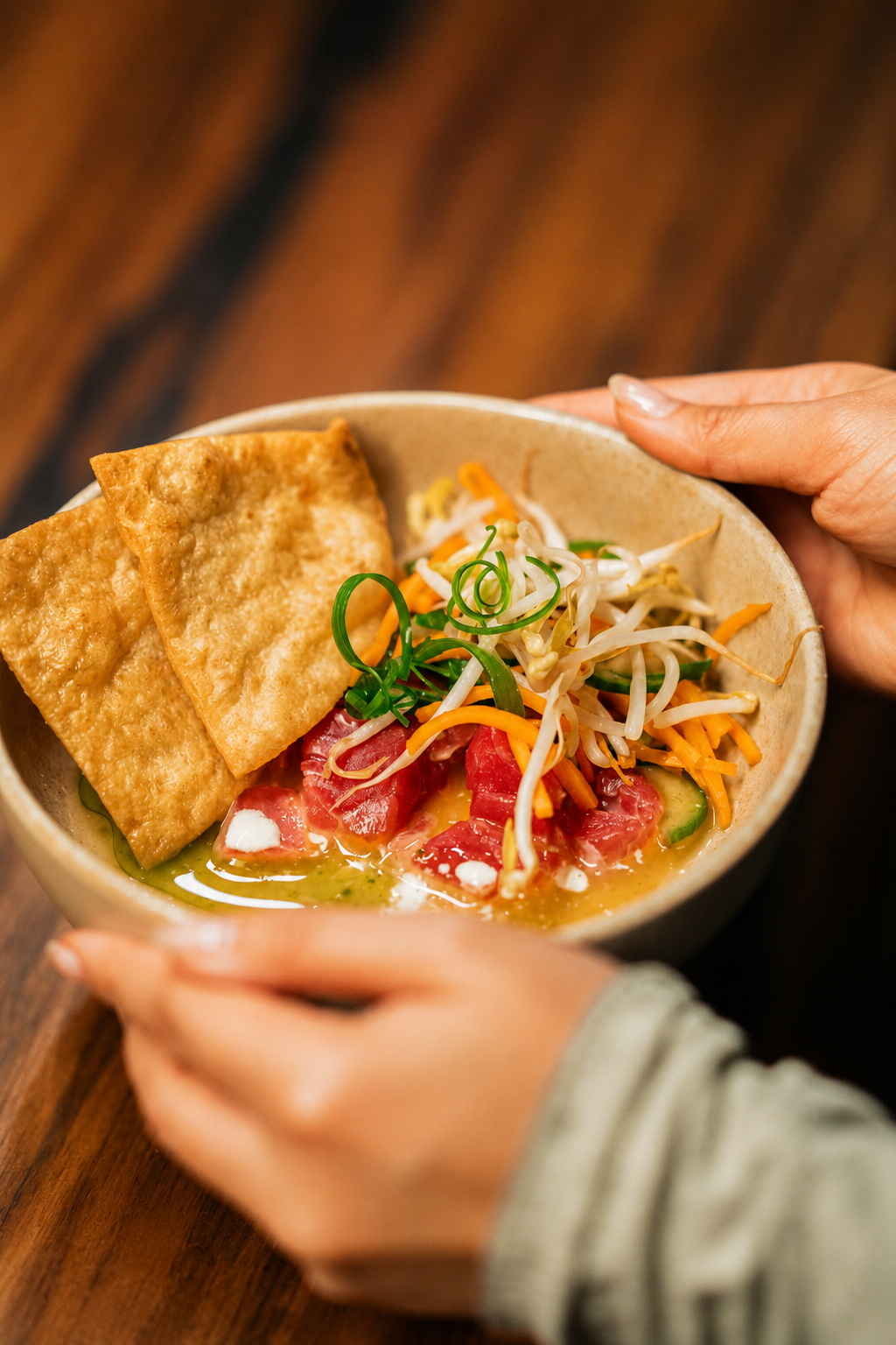 A person holding a bowl of poke with tofu, fresh tuna, shredded carrots, bean sprouts, cucumber, and green onions.
