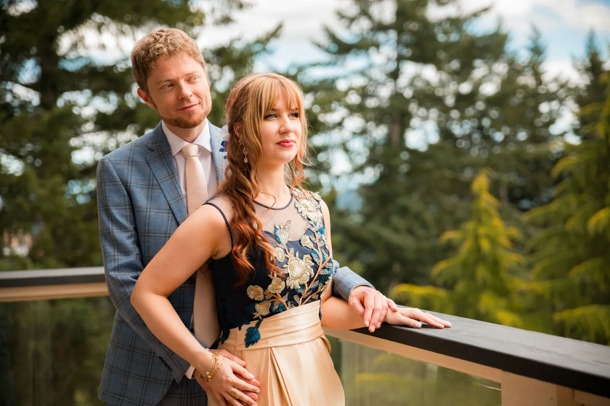 Romantic bride and groom portrait outdoors in Abbotsford BC, with the groom in a blue plaid suit embracing the bride in an elegant embroidered navy and gold dress against a dreamy forest bokeh background. Captured by Shakil Hussain, Abbotsford BC wed