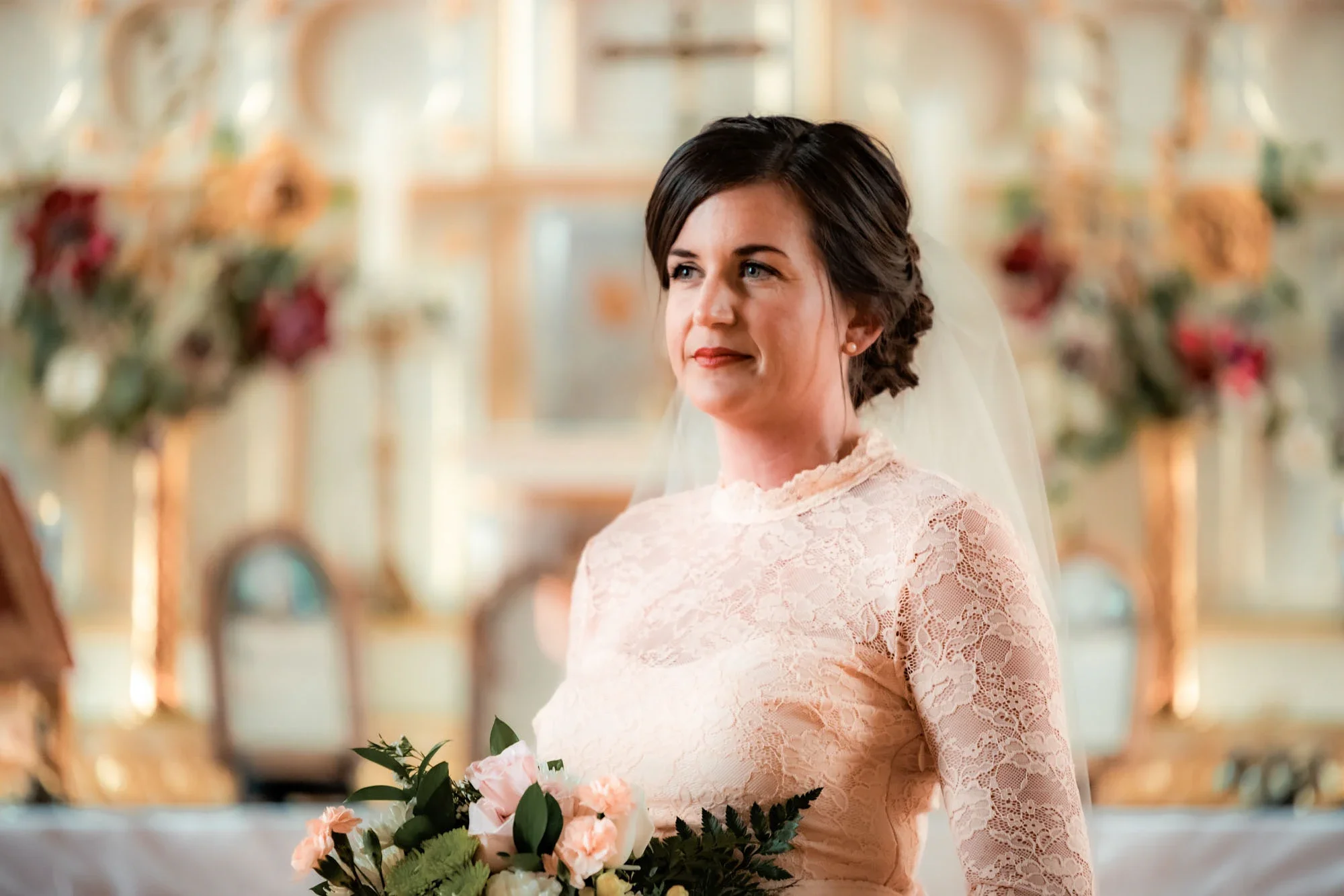 Elegant bride in a blush pink lace wedding gown with veil, holding a soft pastel rose bouquet, captured in a tender moment during her wedding ceremony in Abbotsford, British Columbia.
