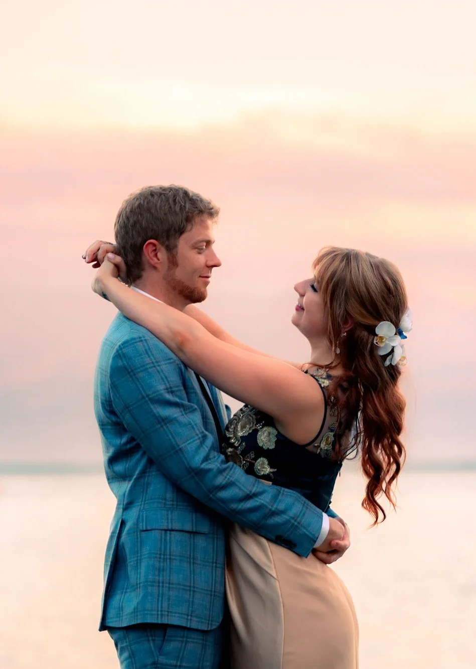 Romantic bride and groom embracing during golden hour sunset on the beach, with soft pink skies and ocean backdrop, captured by an Abbotsford Fraser Valley Vancouver wedding photographer.