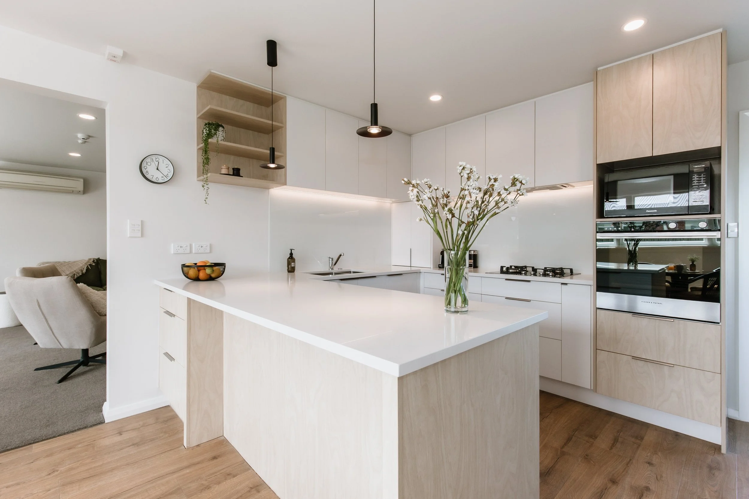 Modern kitchen with white cabinets, a white countertop island, and built-in appliances, including an oven and microwave, with a large vase of flowers as a centerpiece.