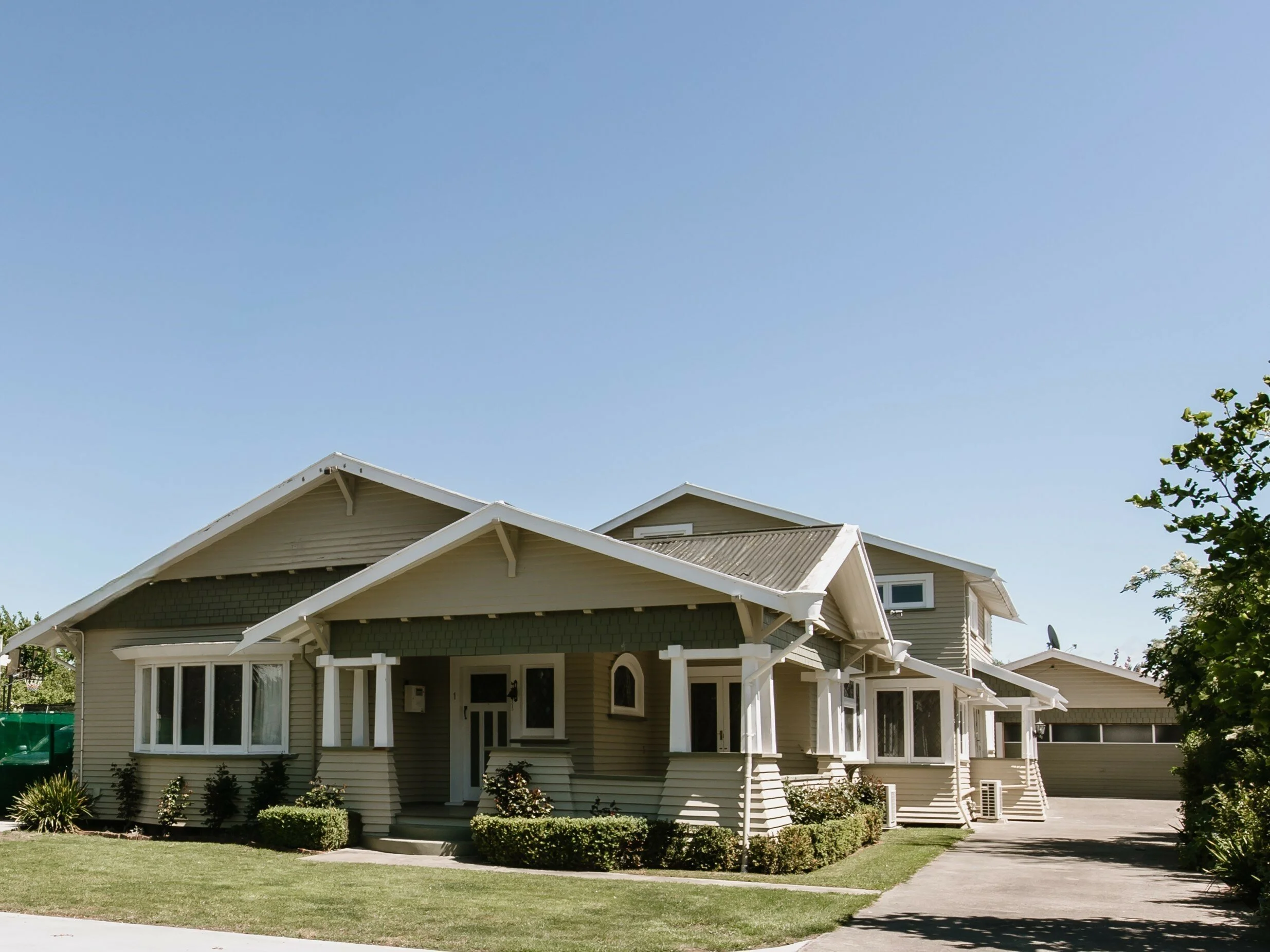 A suburban house with beige siding, white trim, and a well-kept front yard under a clear blue sky.