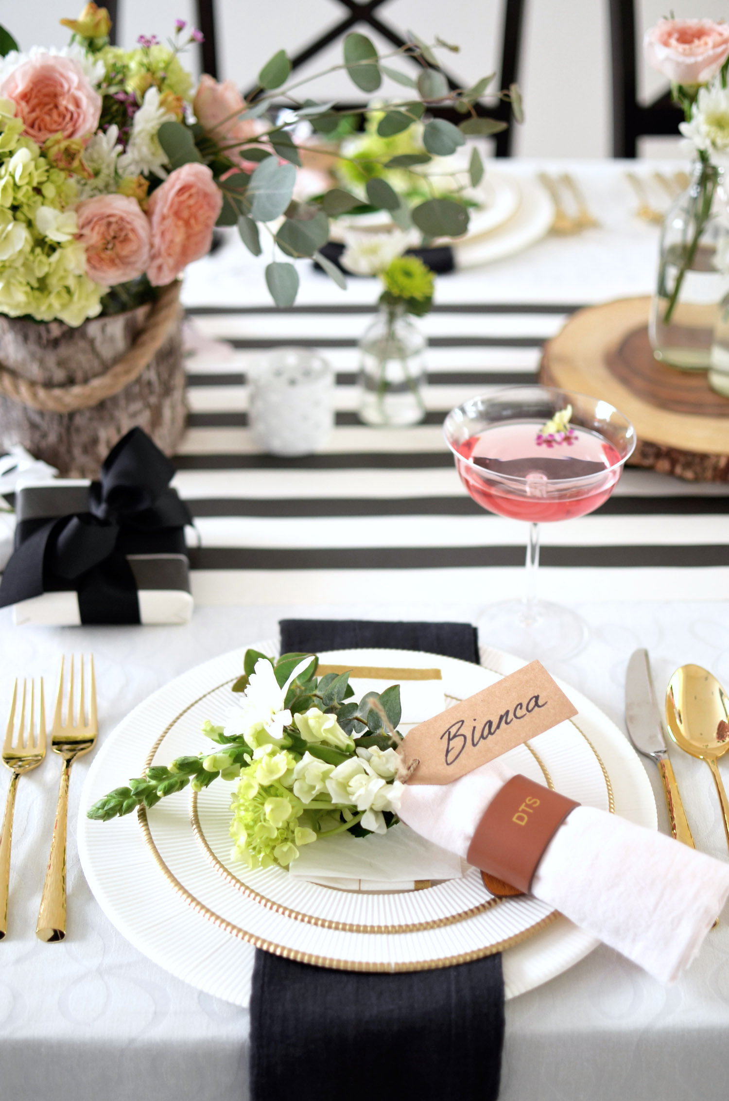  Linens: I was looking for a light background and remembered my kate spade new york ' all wrapped up in bows' off-white tablecloth . I found it at  HomeGoods  and snagged it. I didn't know exactly what I needed it for when I saw it. I just knew I did. It has a delicate pattern of bows and isn't too ivory or too white, but somewhere in between. The color also coordinates with my  black and white striped paper runner  from Hester & Cook and I LOVE the look.  Placesettings: People often ask me how I create a tables that look like this using paper products. Good question. I tell them I set with paper the same way I set with my fine china. It's really that simple. I might be okay using pretty paper 'dinnerware', but I'm not ready to move away from the real deal when it comes to flatware, stemware and accessories on my table. For this setting, I layered the  Ivory & Classic Gold Collection  from Sophistiplate. This 44-piece set and service for eight that includes  charger plates ,  dinner plates ,  salad/dessert plates ,  appetizer/dessert bowls  and  napkins . I mixed and matched solid white pieces, along with gold edged pieces mirroring the way I would set my fine white china and accent plates. Under the dinner plate, I added a black flour sack napkin (from my friends at  Merc Textile  - who hand make the cutest towels!) to add some color to the placesetting, and topped the settings with mini-bouquets for each guest, that also doubled as place cards. I wrapped a pink flour sack napkin around the bouquet to keep it looking pretty (and the stems neat!). To keep it all together, I added  monogrammed leather napkin rings  from Mark and Graham and accented the placesettings with my  gold flatware  from  Marchesa by Lenox .  Cocktails or Wine: With a placesetting this sweet, I knew a glass of rosé was (clearly) in order and it needed to be in the perfect  coupe , topped with edible flowers. My version of the word 'perfect' here are these  stemmed cocktail glasses  (yep, Mark and Graham!). Of course, there is always plenty of champagne on ice at my house and...wine. 