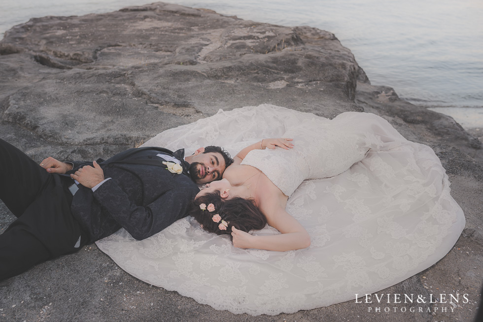 stunning bride and groom laying on rock St Heliers beach {Auckland-Hamilton-Tauranga wedding photographer}