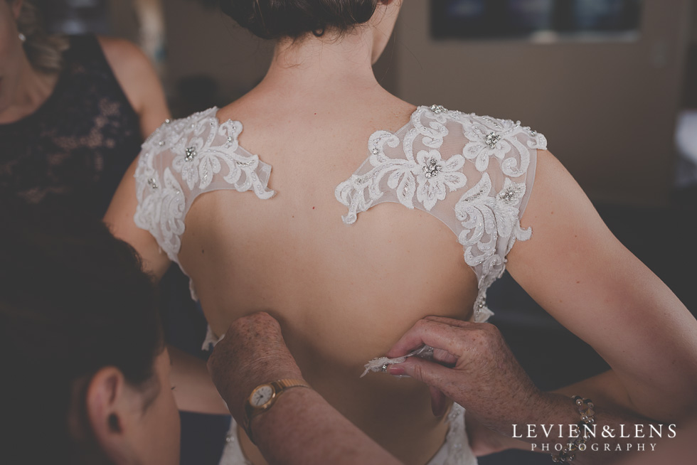 bride getting ready putting dress on Castaways Resort - Kariotahi beach wedding {Auckland lifestyle couples-engagement photographer}