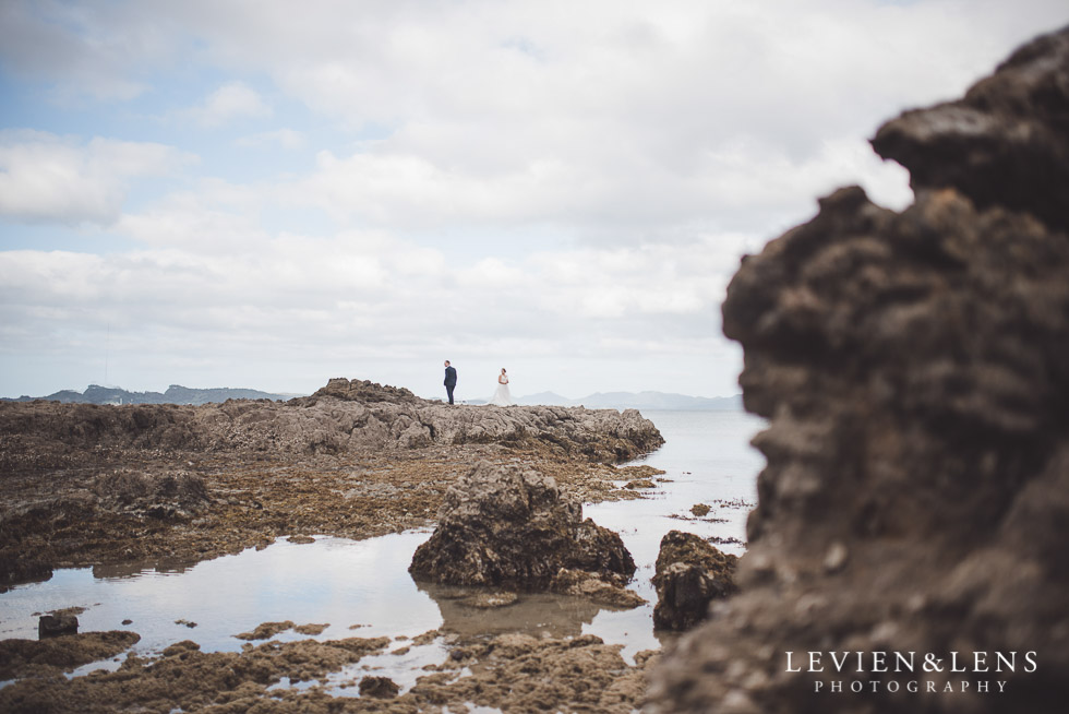 bride and groom walking on rocks far - beach - The Duke of Marlborough Hotel - Russel wedding {Northland-New Zealand weddings photographer}