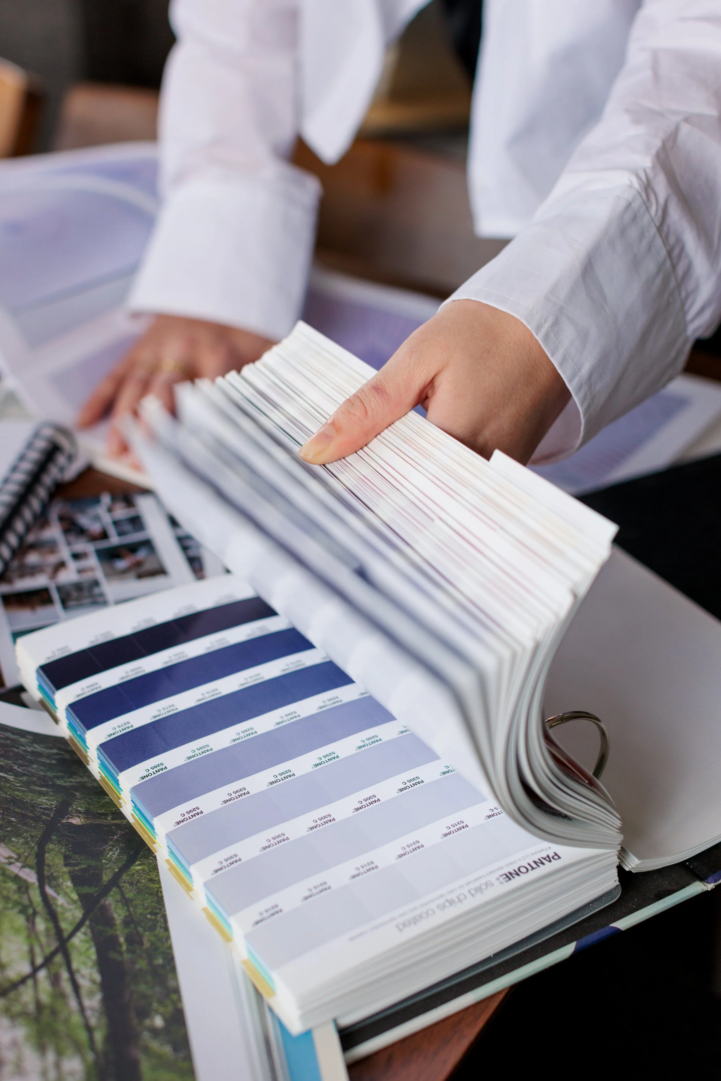 Person flipping through a color swatch book with paint color samples and catalog pages on a table.
