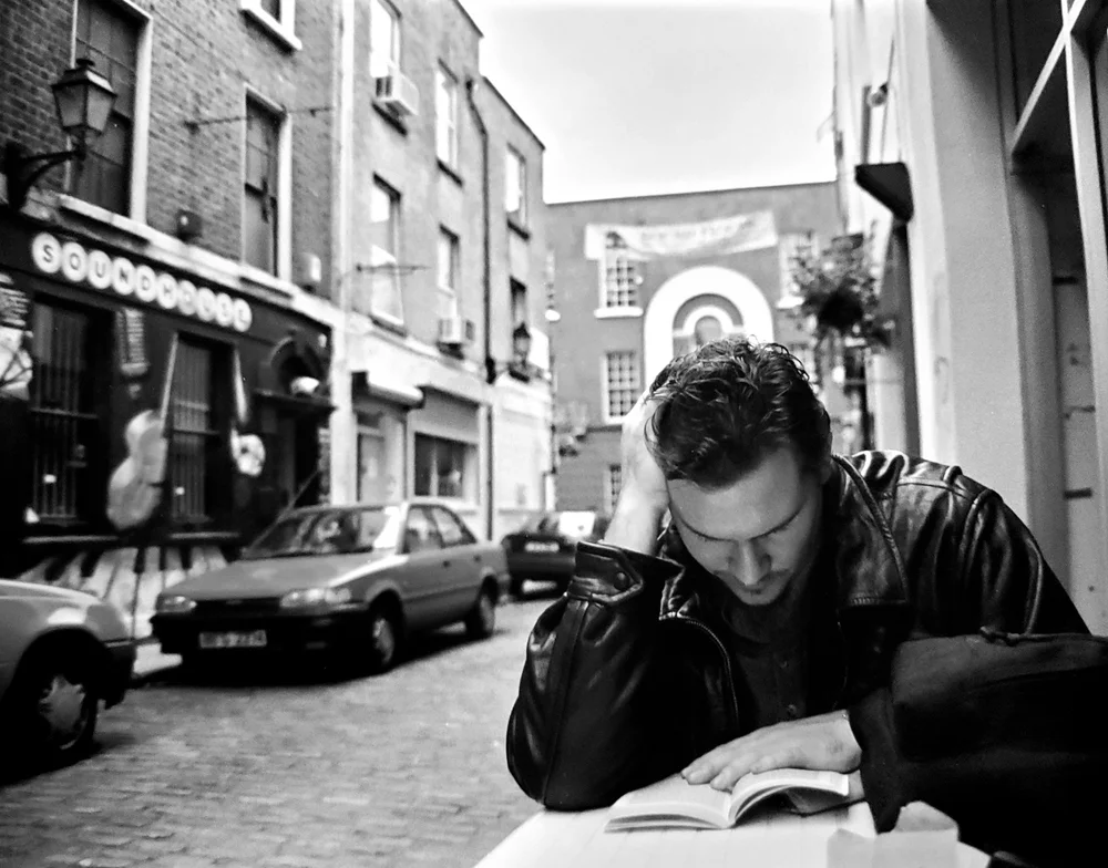 Hosho McCreesh reading at a table on a cobblestone street in Dublin, black and white
