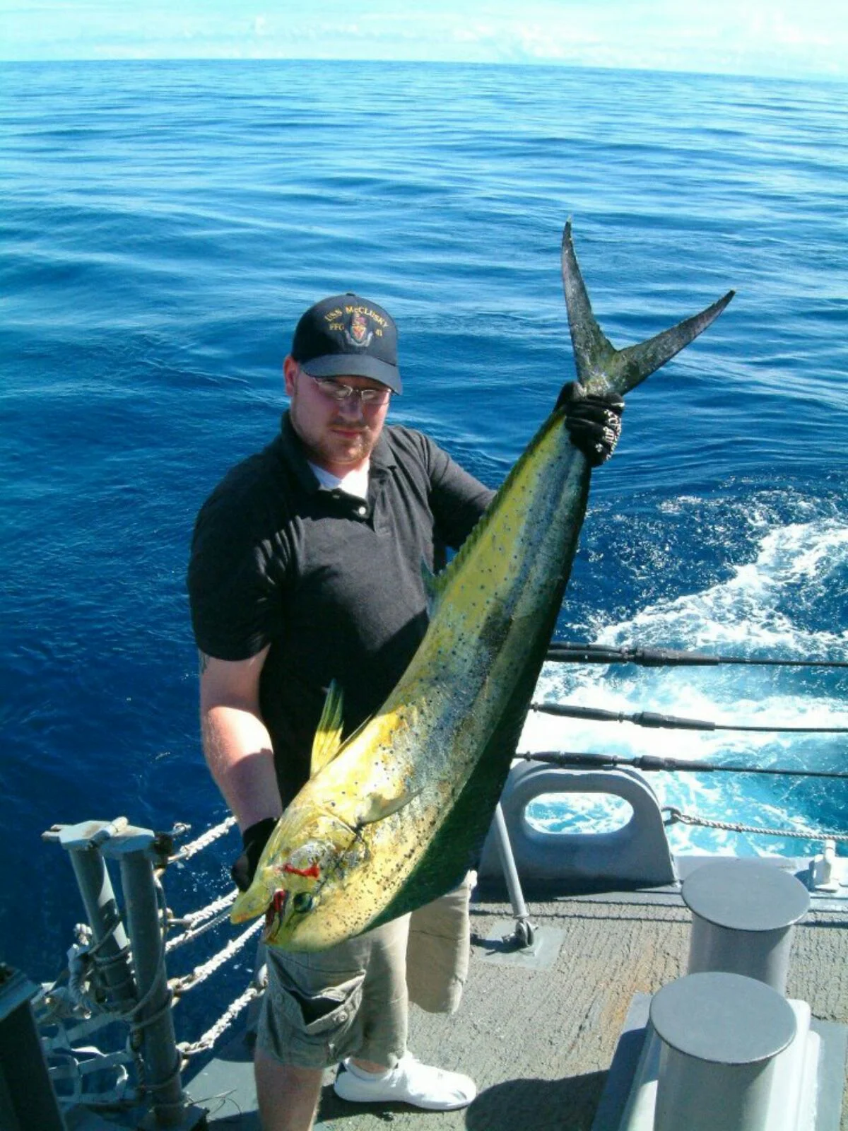 Man in Navy catches Mahi off of Ship's stern