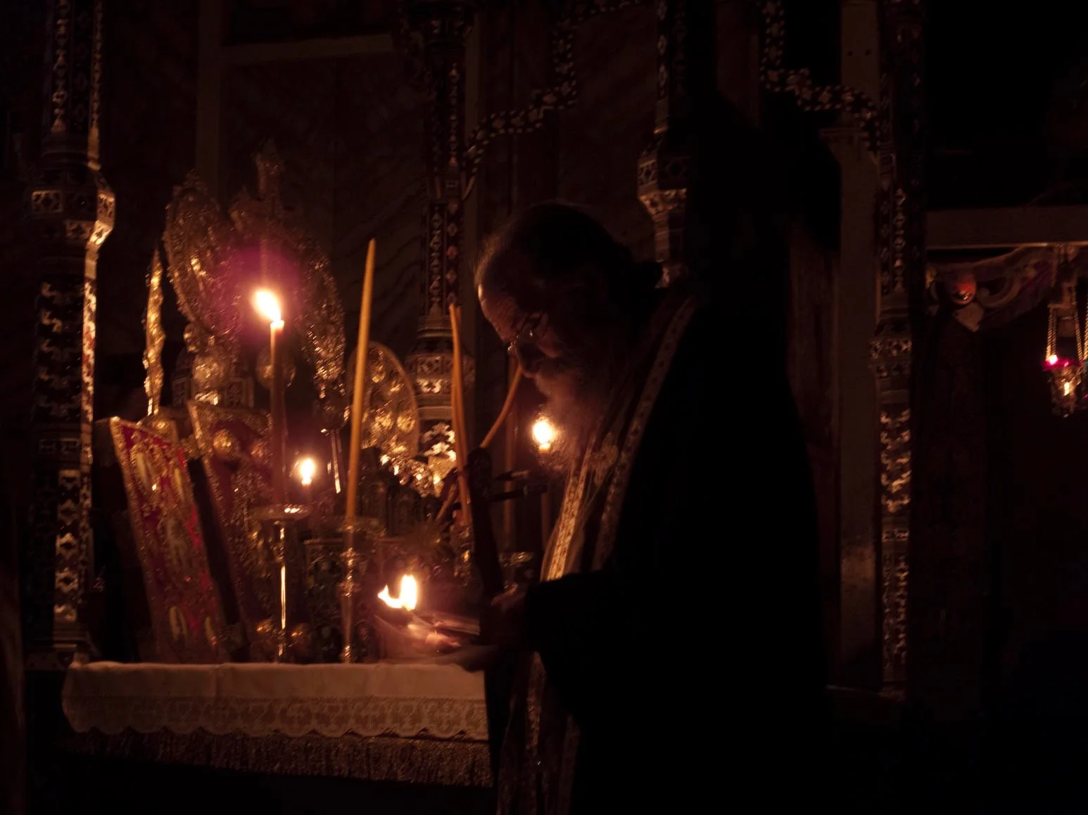 At the holy altar on the Feast of the Saint, Father Pavlos borrows the glow of a few tapers to read names of those who have sought his prayers.