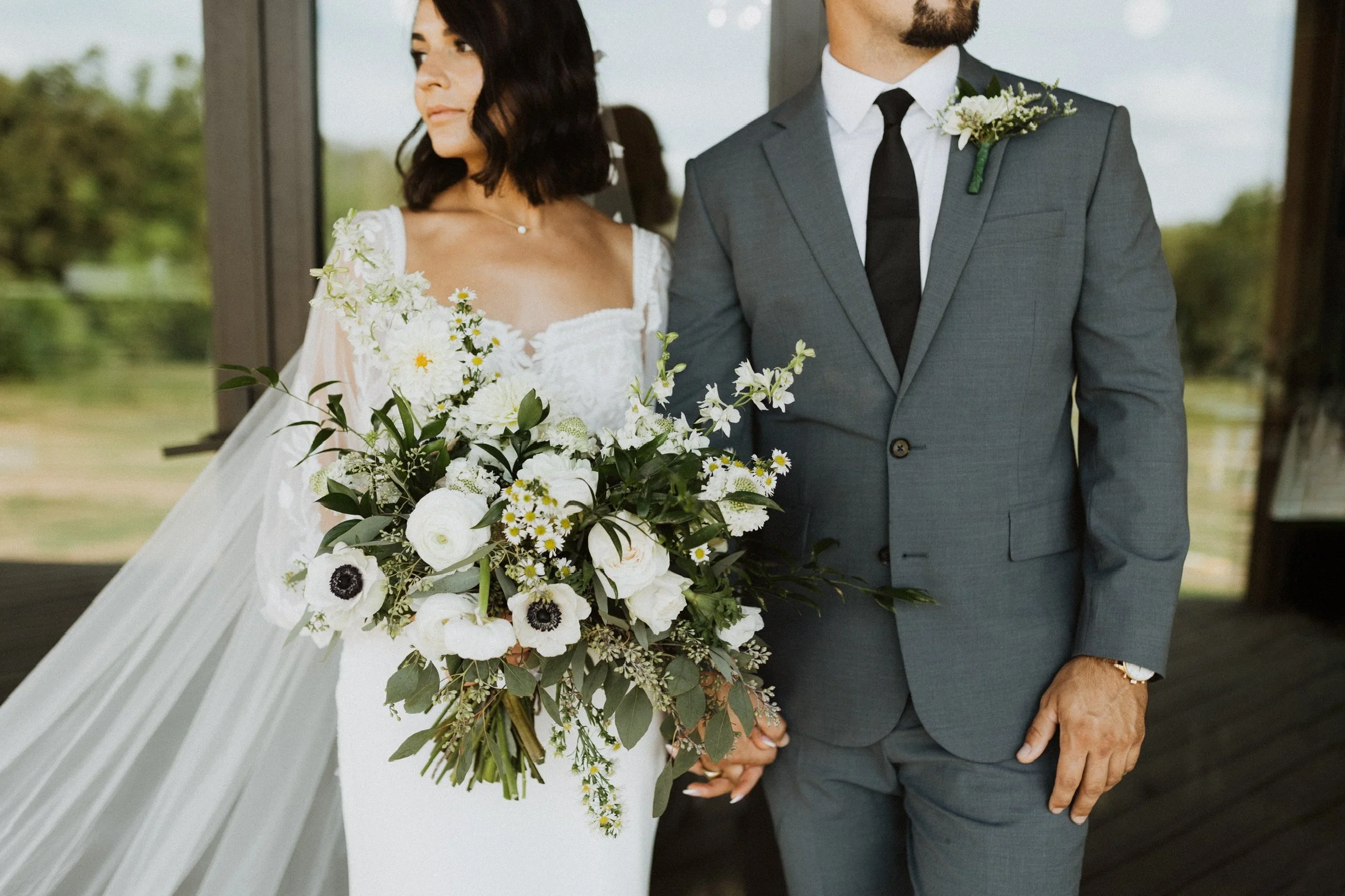 Stella Blue Design bride and groom Lana and Alex pose during their first-look photo shoot. Lana wears a 14K yellow gold necklace featuring a single stationed round diamond and holds a cascading white floral bouquet.