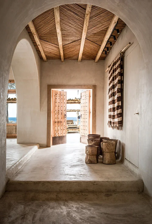 I love the juxtaposition between the cement floors, plaster walls, and unique wood ceiling pattern in this room. And what beautiful doors! 