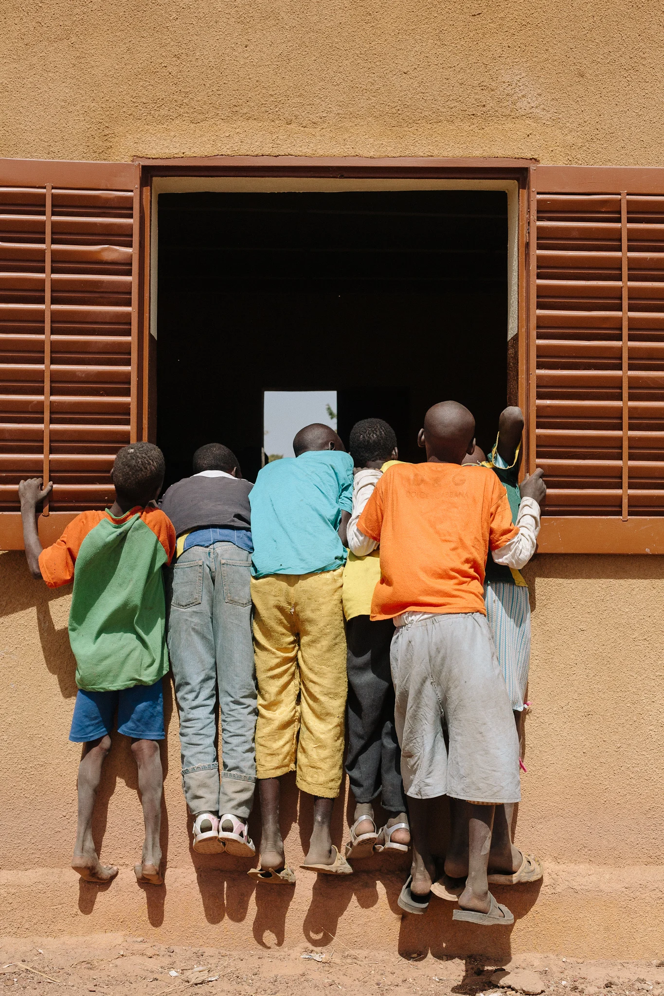 In the village of Gnenkekoro, children hang from a school windowsill in order to observe the dental clinic taking place inside.