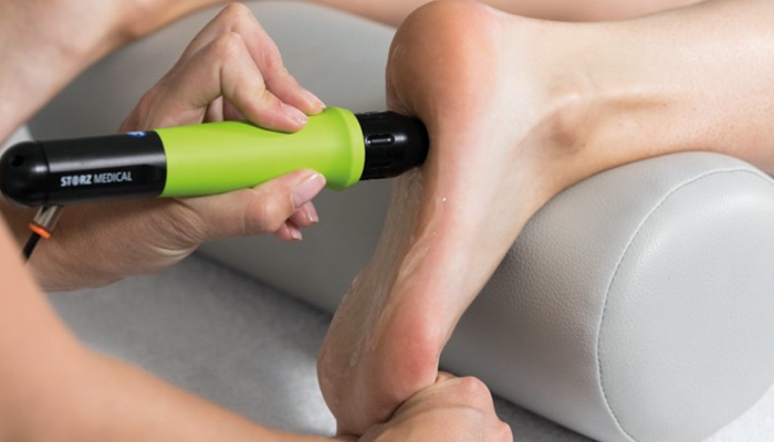 A chiropractor applying shockwave therapy to a patient's heel for plantar fasciitis treatment at Revive Sport & Spine in Murray, Utah.