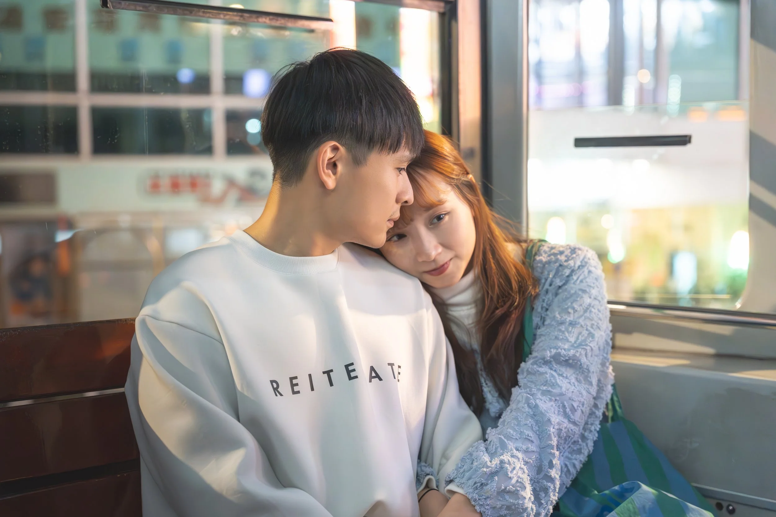 A young man and woman sitting close together on a bus, with the woman resting her head on the man's shoulder.