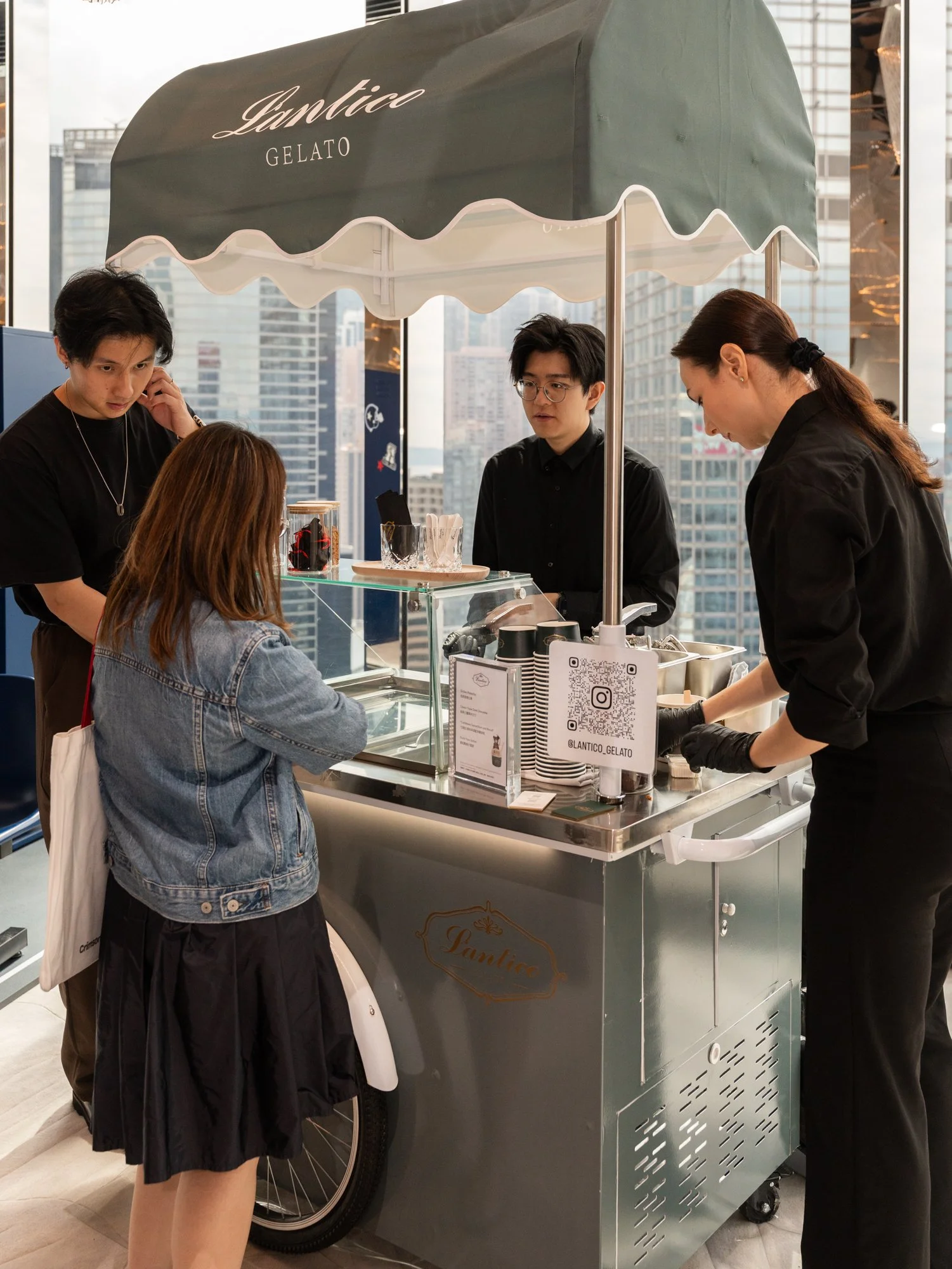 People ordering gelato at a gelato stand in a city with tall skyscrapers in the background.