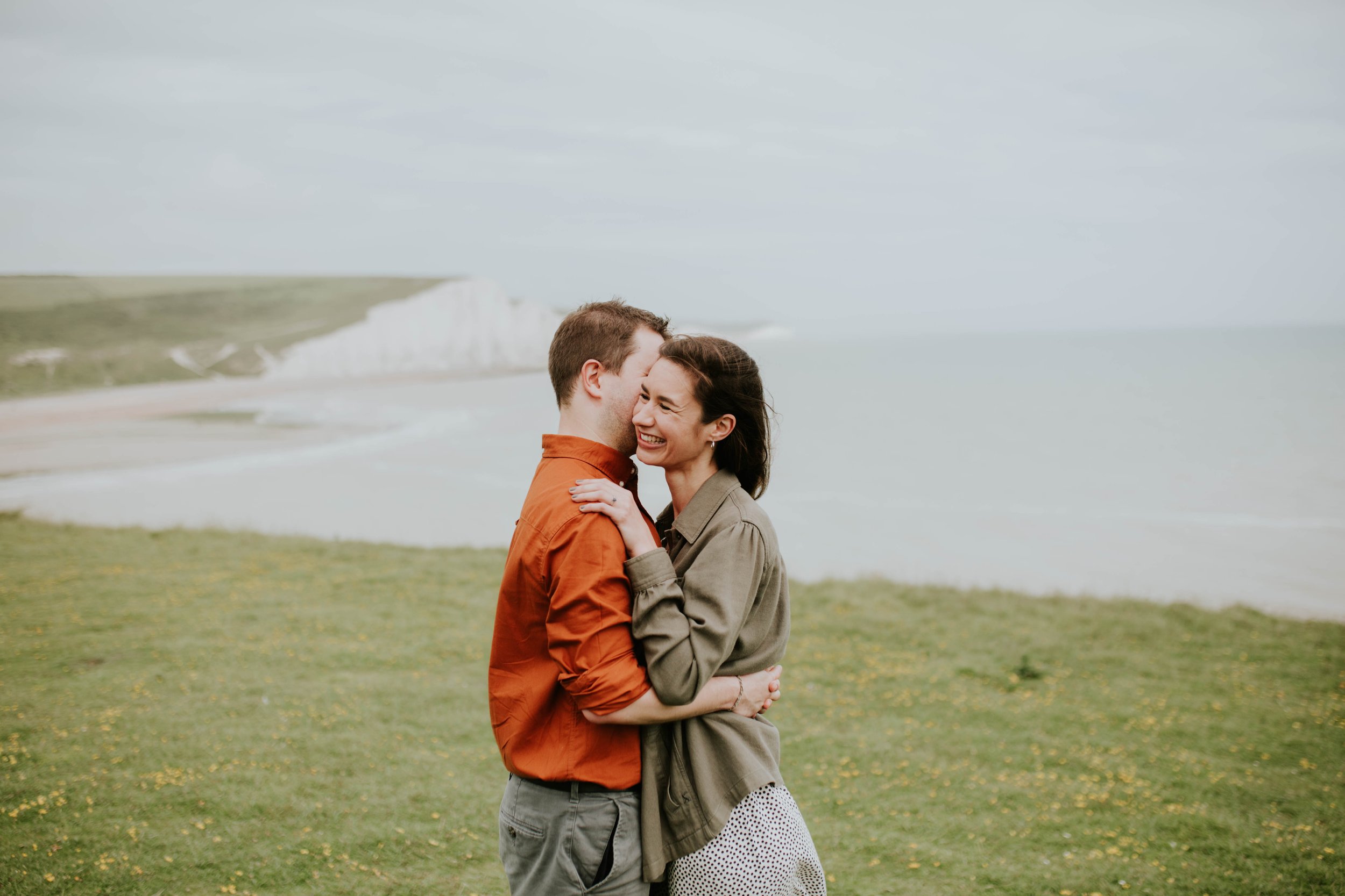 An engaged couple share a kiss on the cheek.