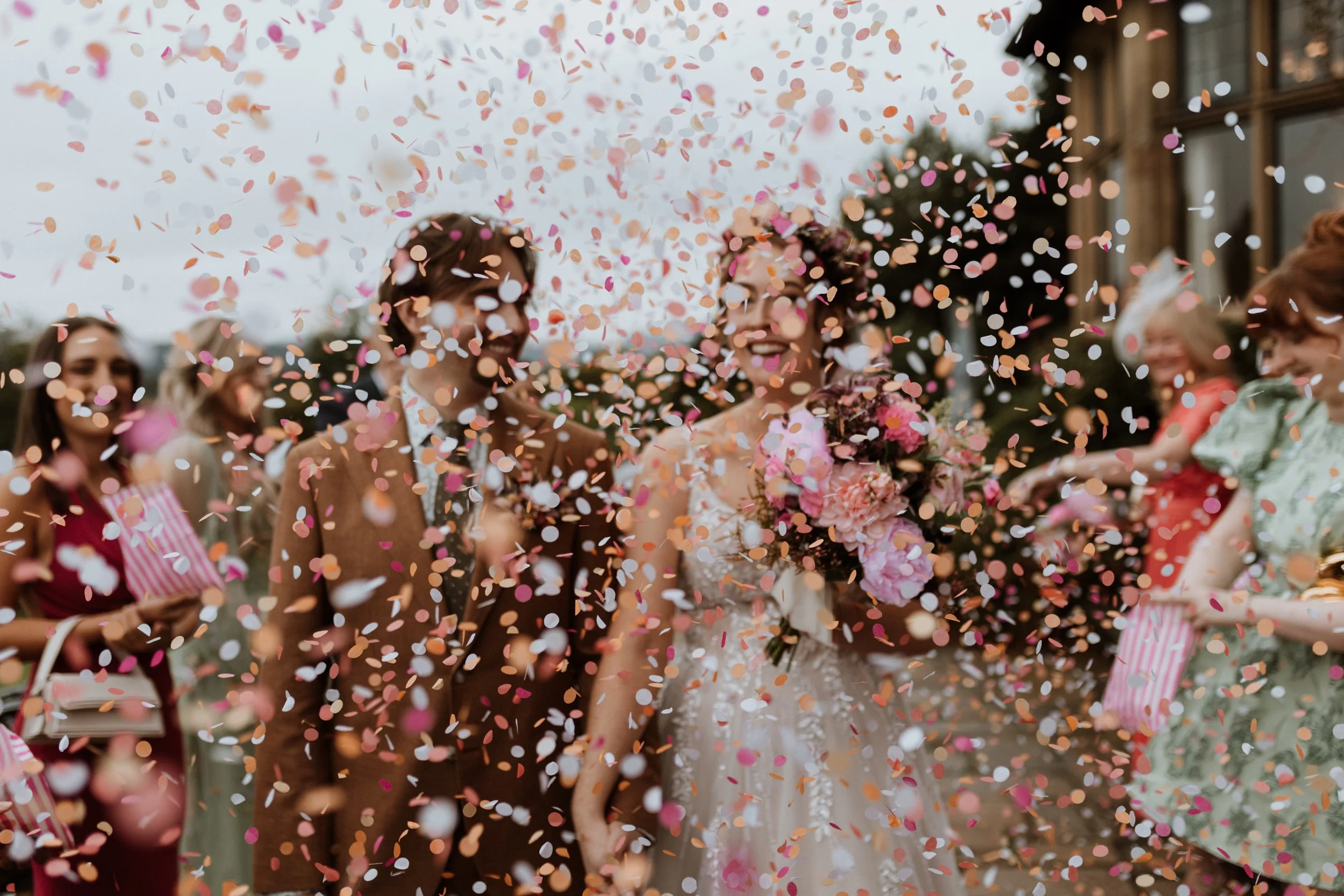  Pink and yellow paper confetti falls as a bride and groom walk together in the Lake District.  