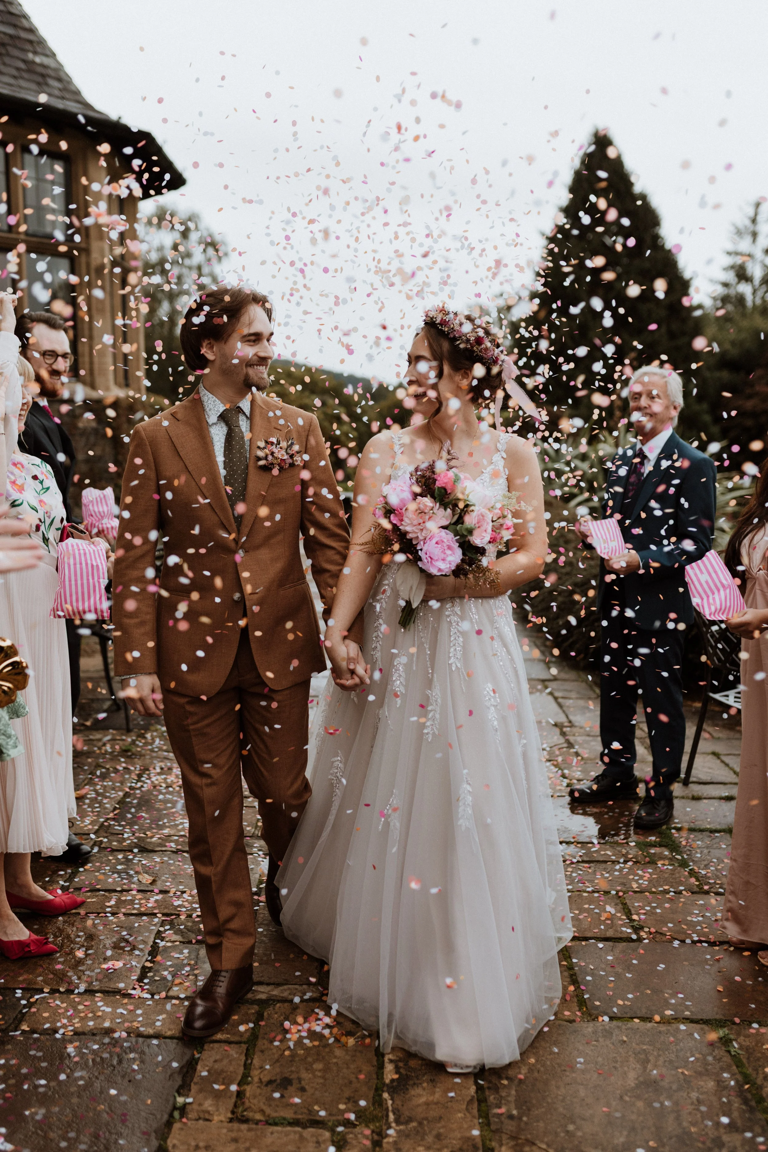  A bride and groom hold hands and walk through their confetti tunnel in the Lake District.  