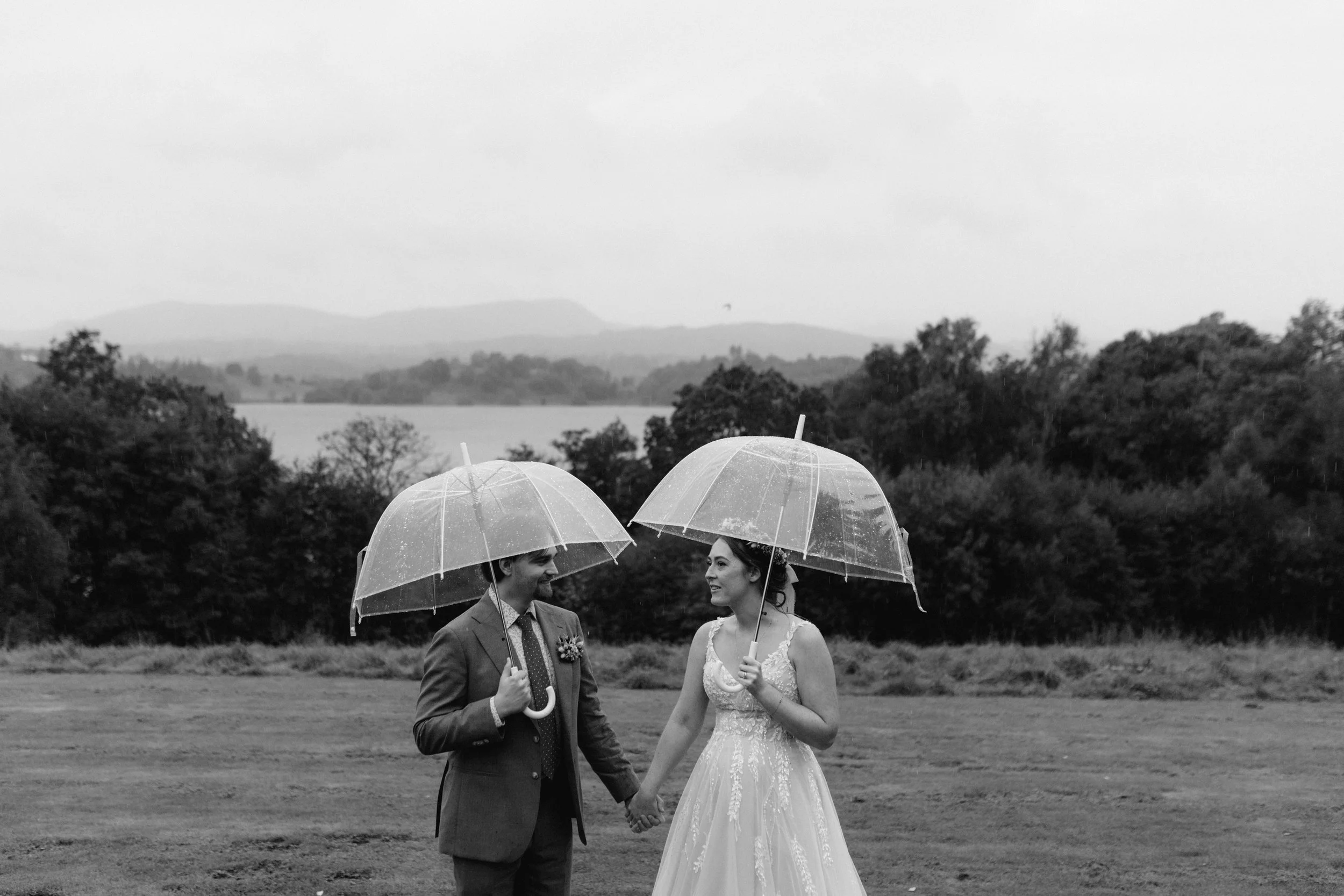  A black and white image of a bride and groom under an umbrella during a rainy Lake District wedding. 