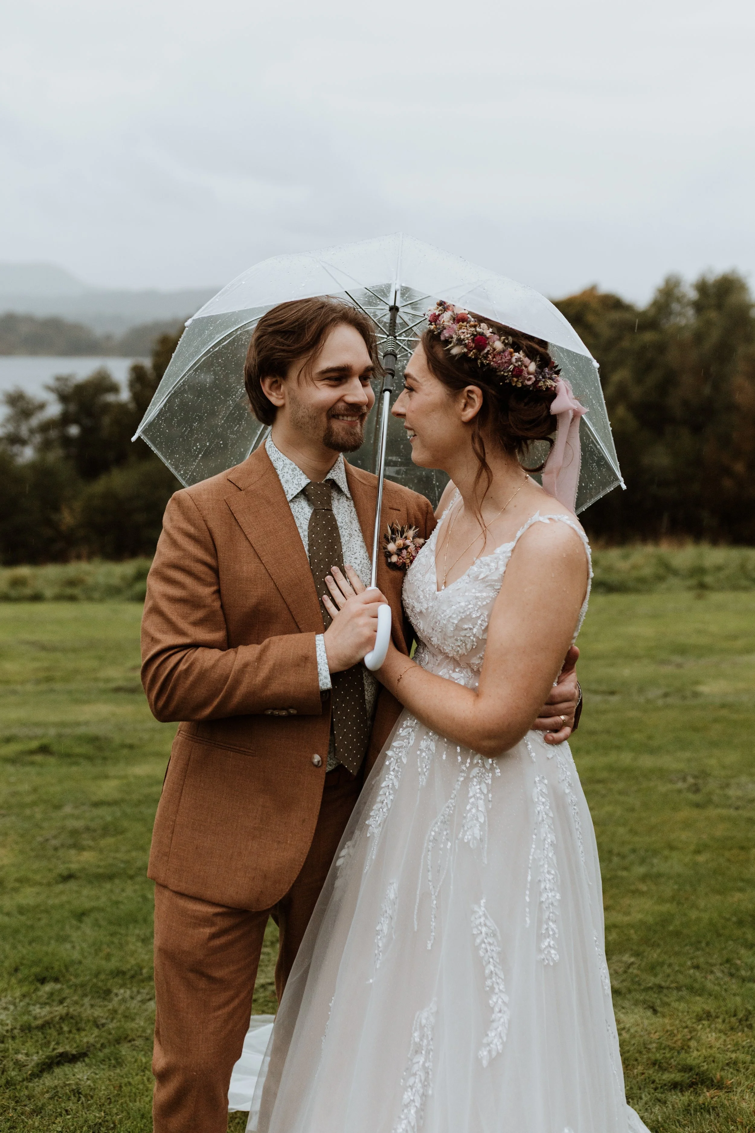  A bride and groom cuddle under an umbrella during a rainy Lake District wedding. 