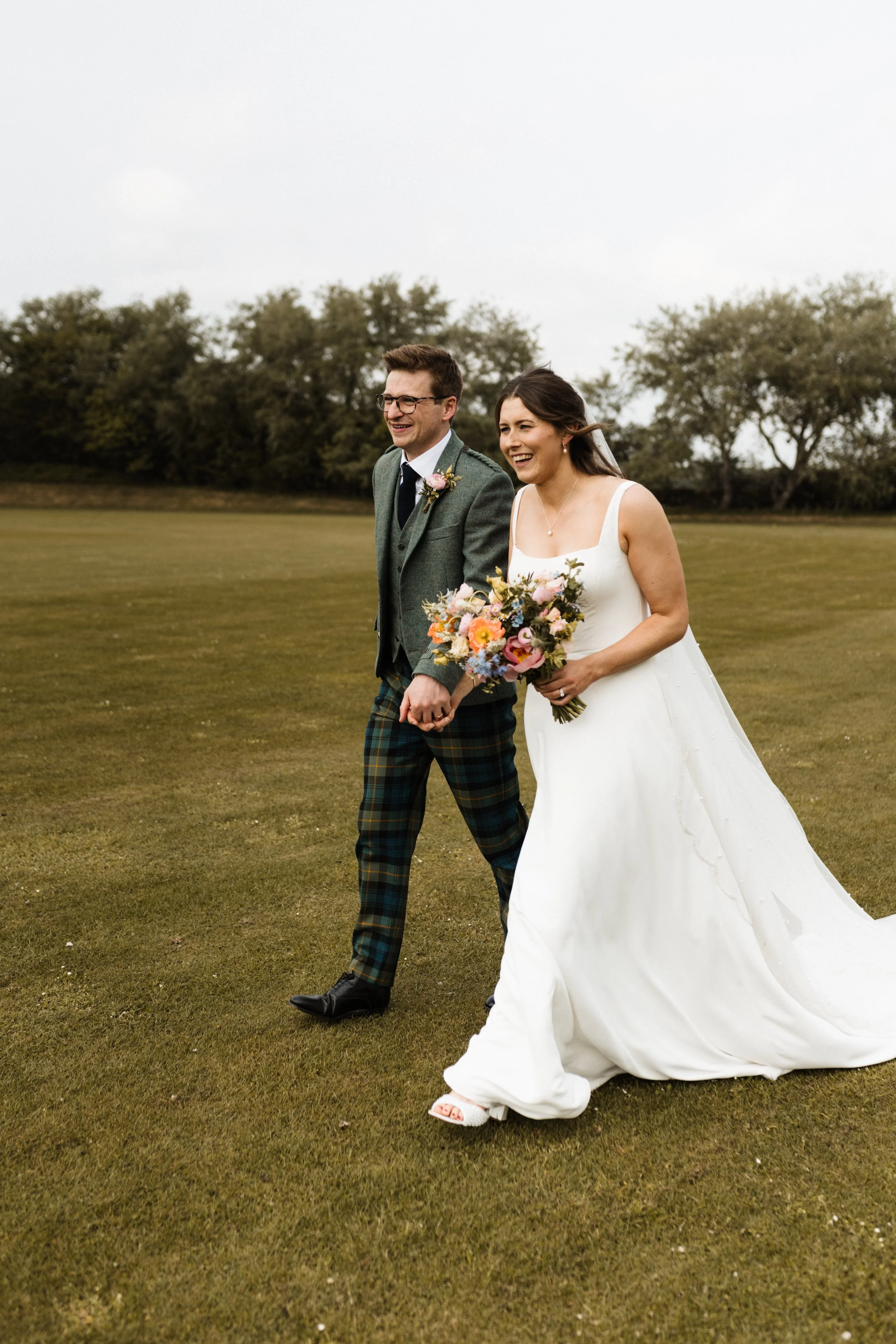 A birde and groom hold hands as they walk together.