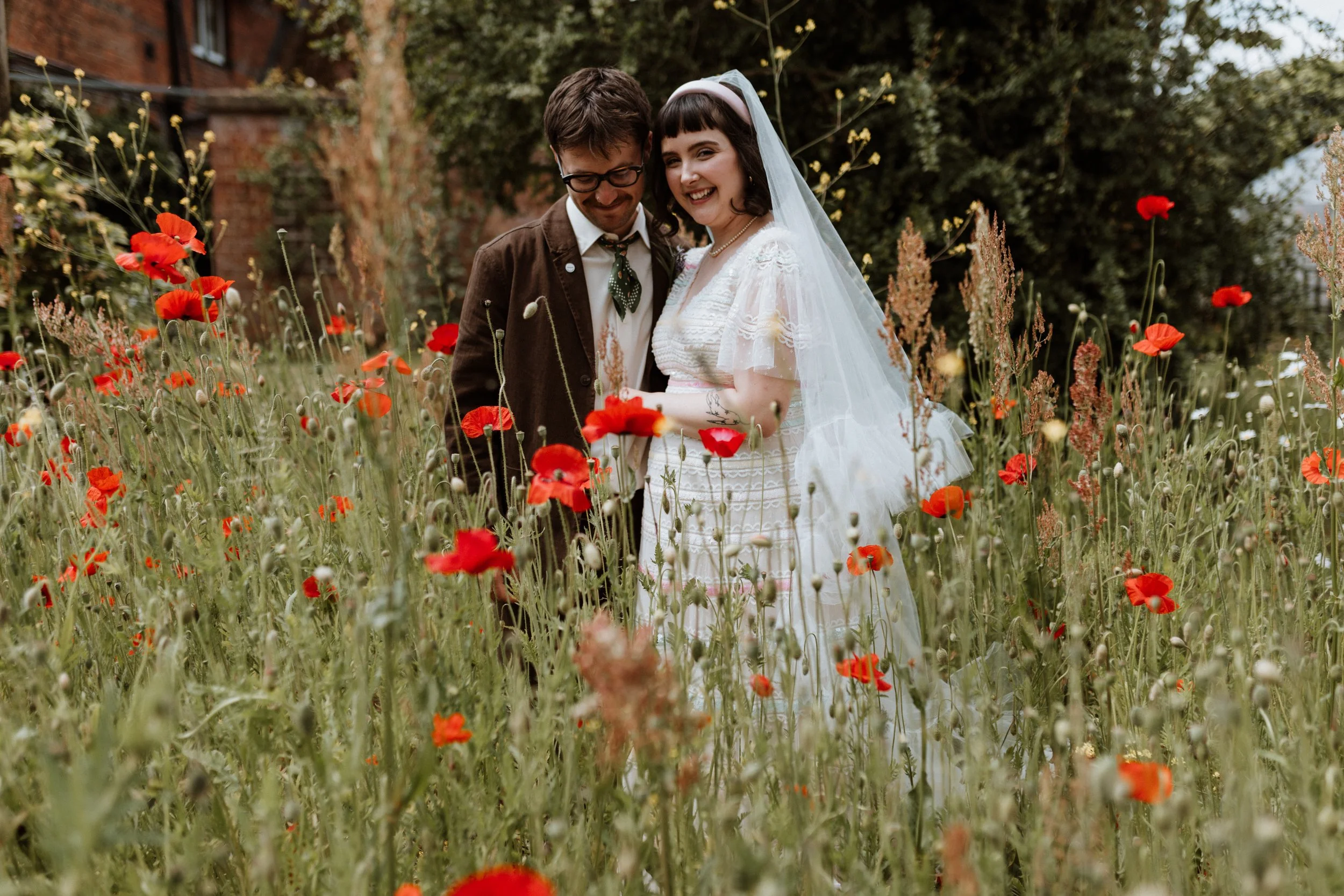 In a field of Poppies, a bride and groom stand together for a portrait.