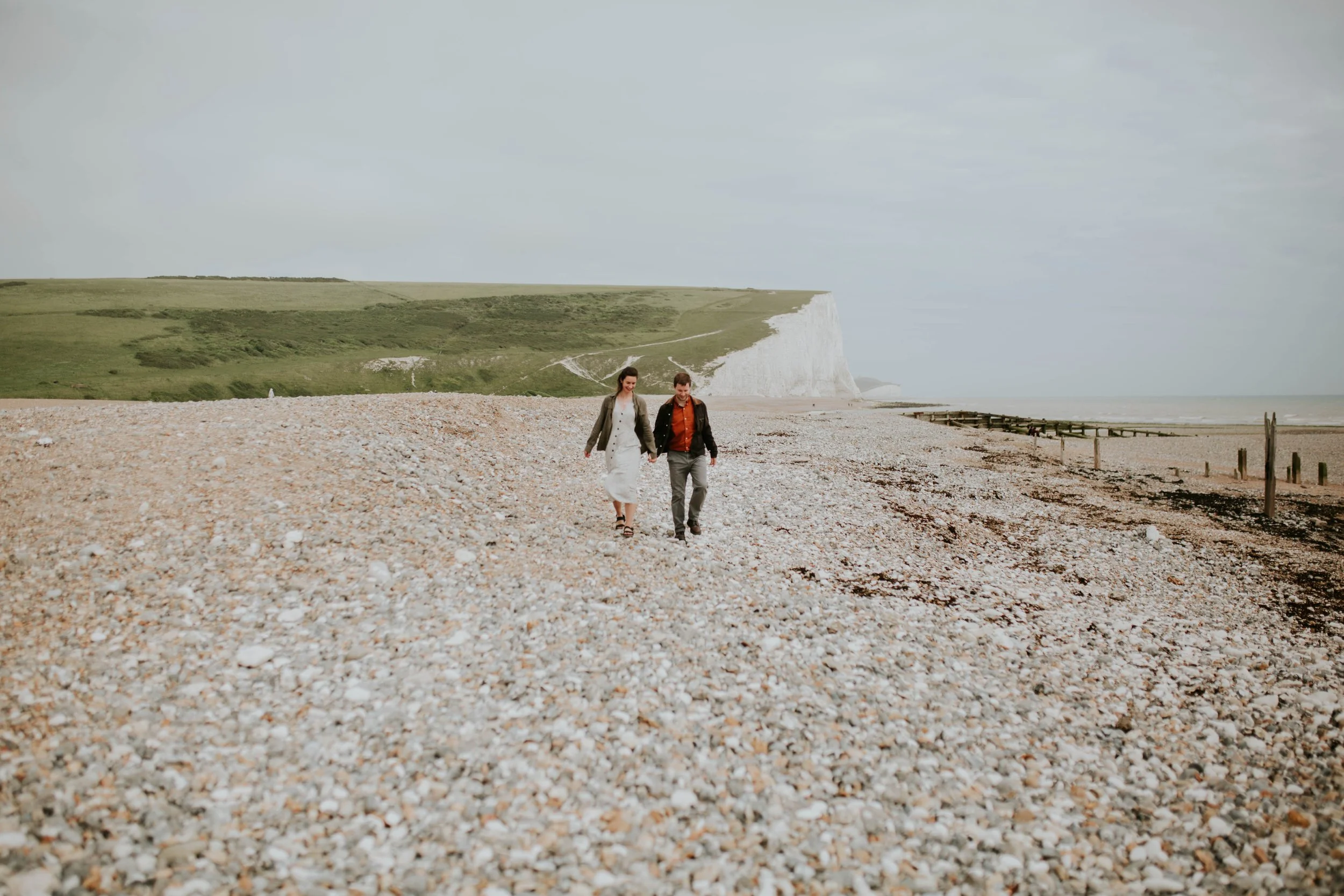a couple newly engaged walk along a beach together.