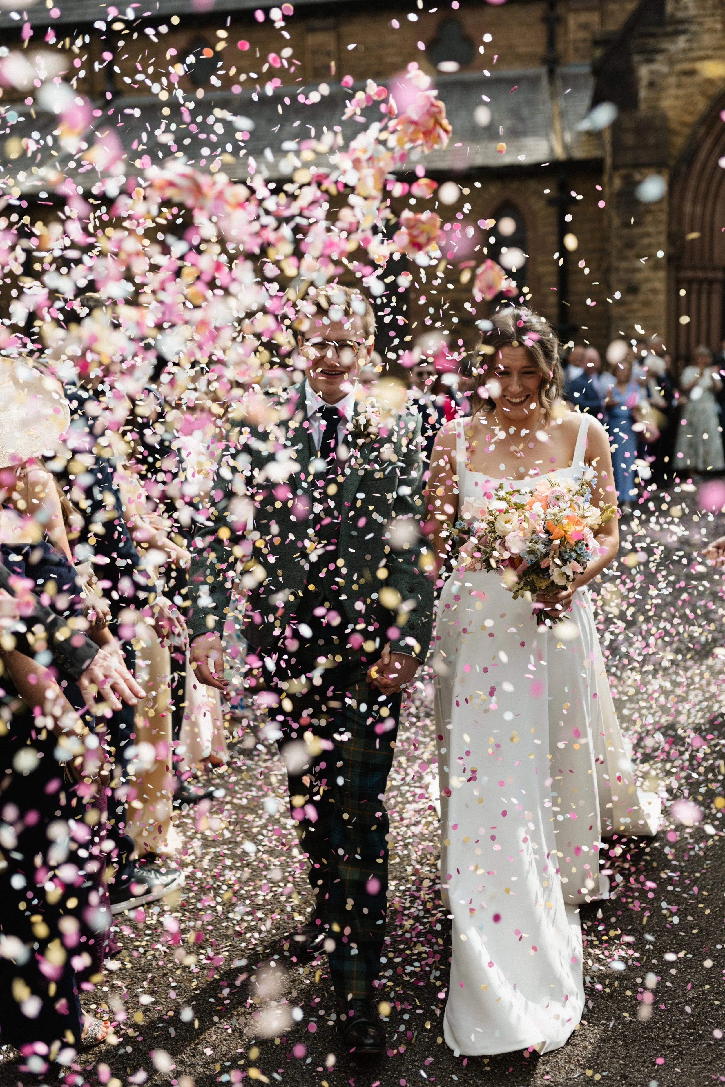 A bride and groom walk through a shower of paper confetti outside a church in Liverpool.