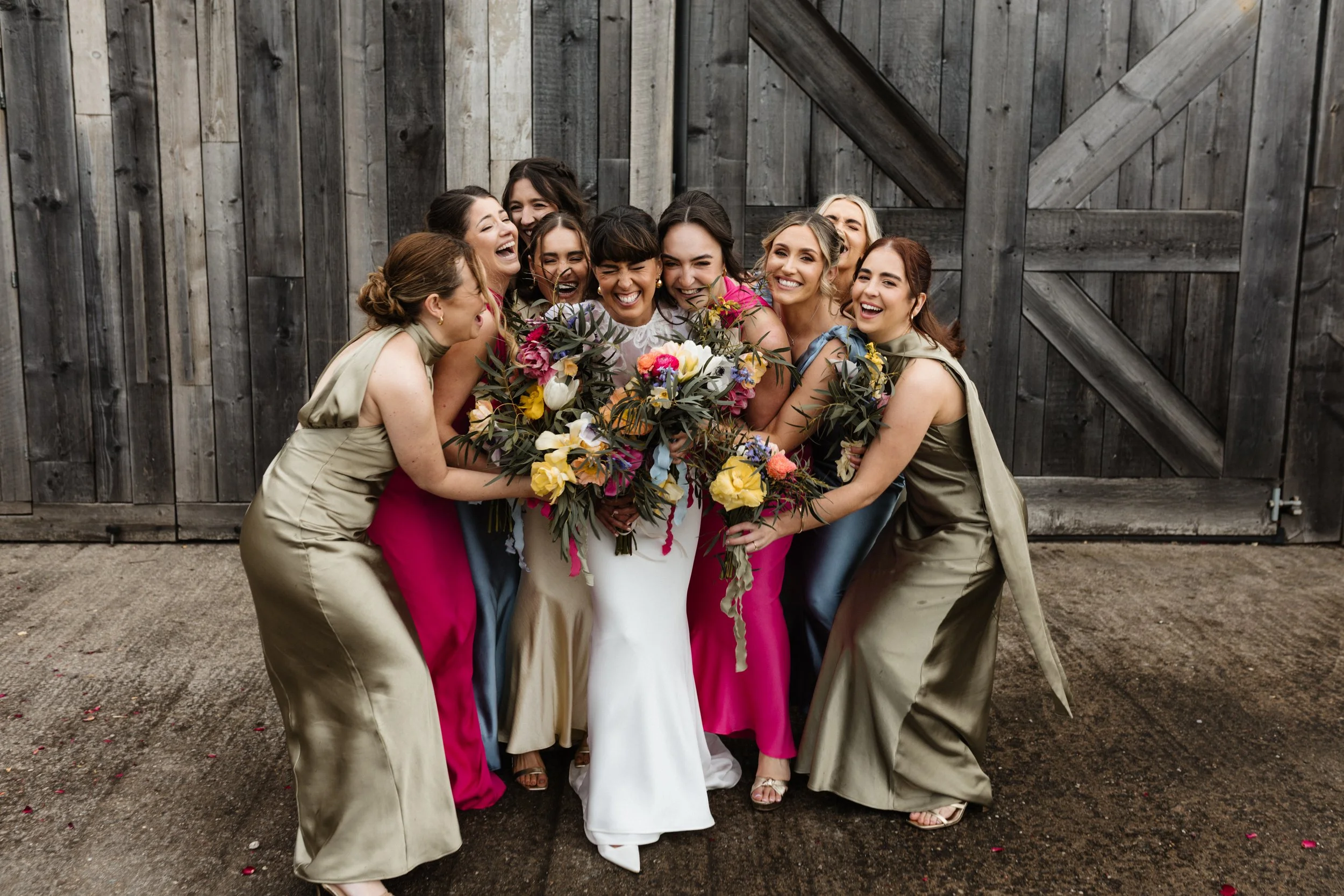 A bride is hugged by her bridesmaids on her wedding day, outside the Grange Barn.