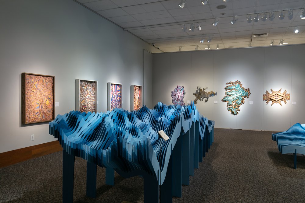 View showing "Sneffles Skyline" in the foreground, a series of ractangular altered topographic sculptures on the left wall, and a series of non rectangular sculptures on the right wall