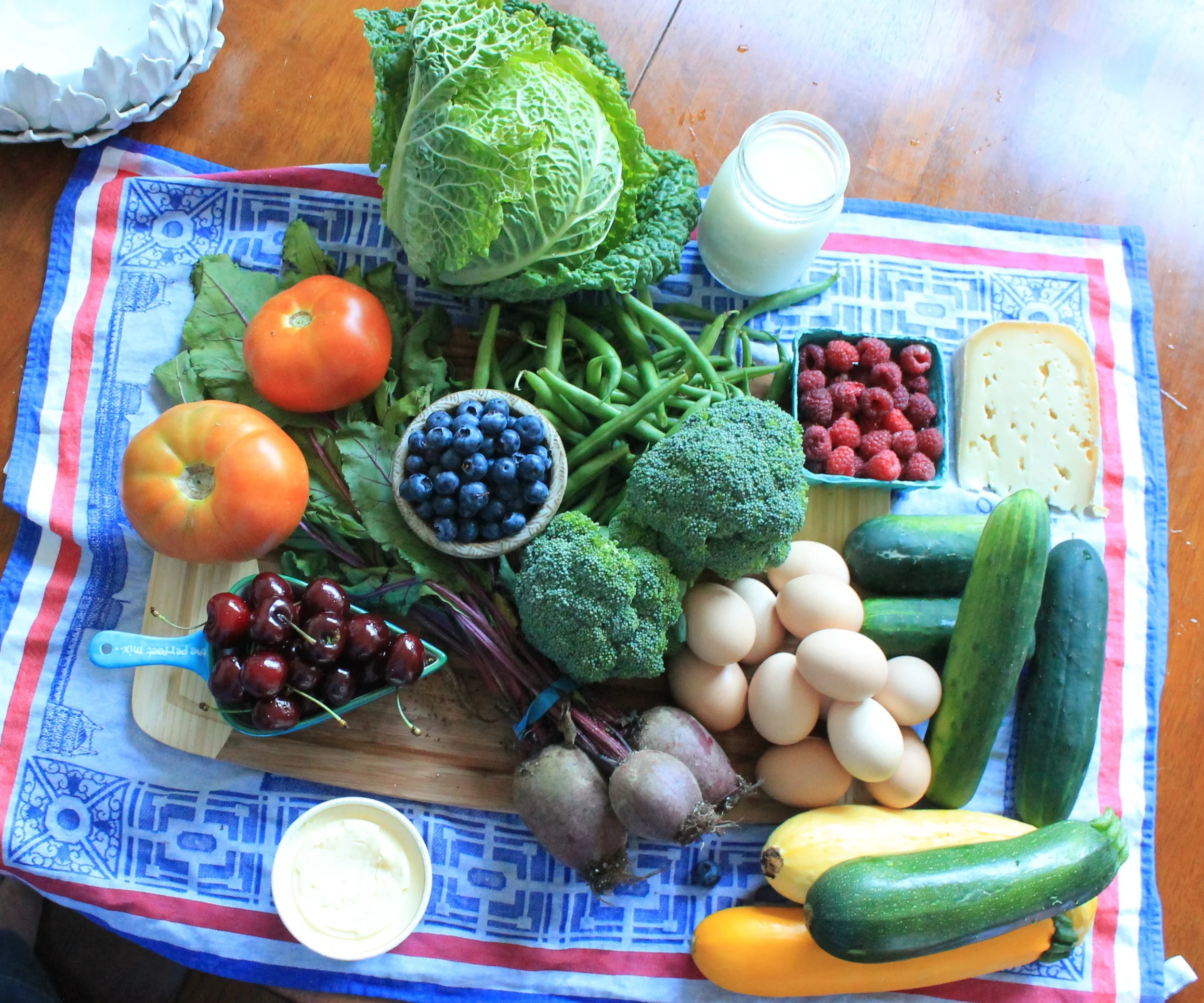 From 12 o'clock: savoy cabbage, the best milk maybe ever, green beans, red raspberries, kind of mind blowingly good swiss cheese, kirby cucumbers, regular cucumbers, eggs, yellow summer squash, green zucchini, yellow zucchini, beets, broccoli crowns, blueberries, butter, cherries, tomatoes. Not shown is Yoni's chocolate milk. We also have yogurt from last time. We're gonna have some good eats these weeks. 