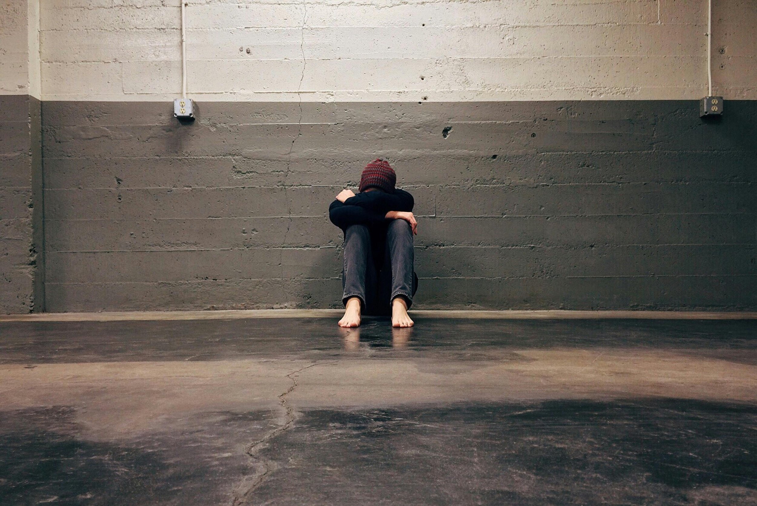 Person sitting against a wall with head down, conveying emotional distress