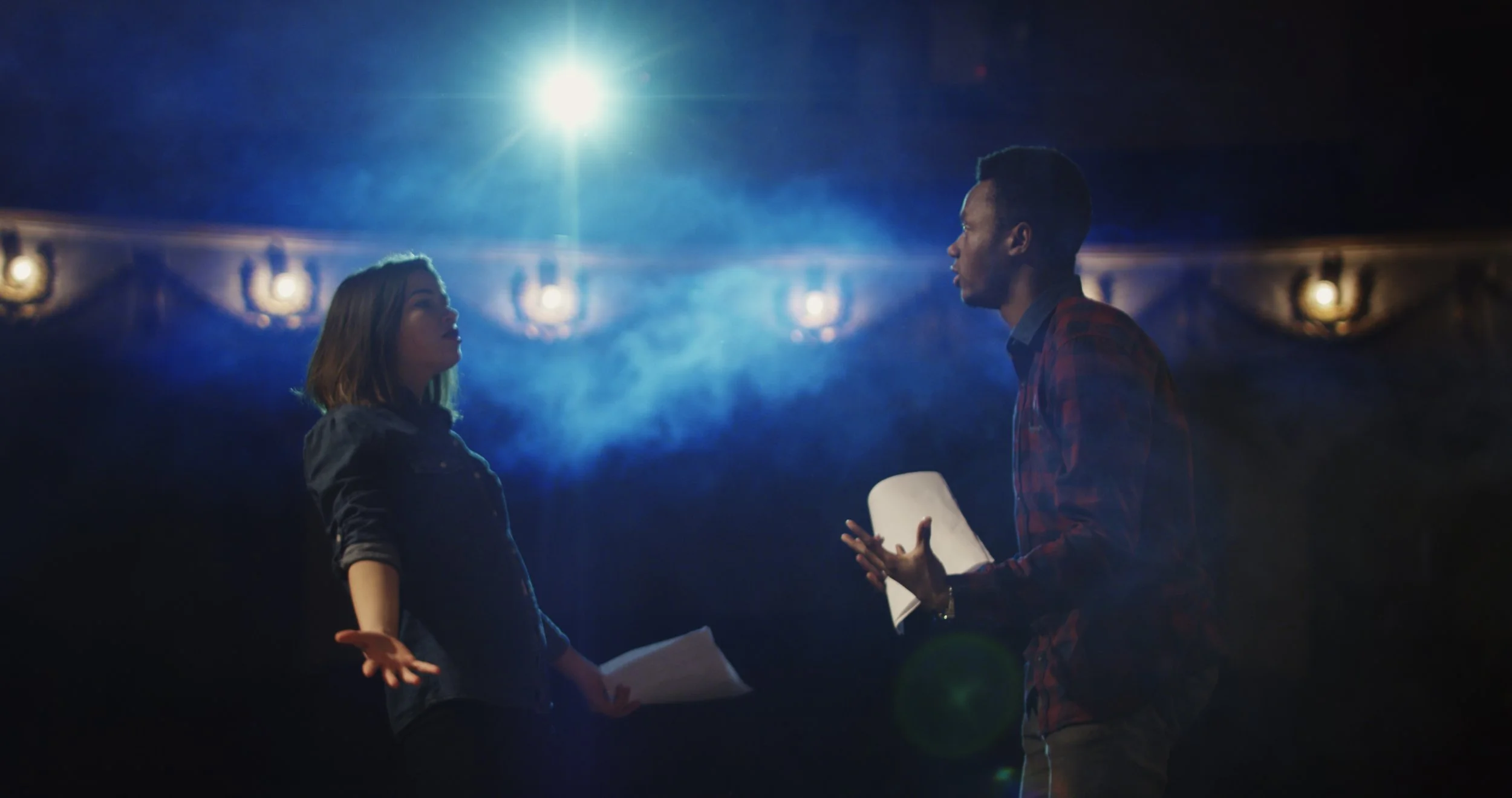 n actor and actress rehearsing a scene in the theater while holding their scripts