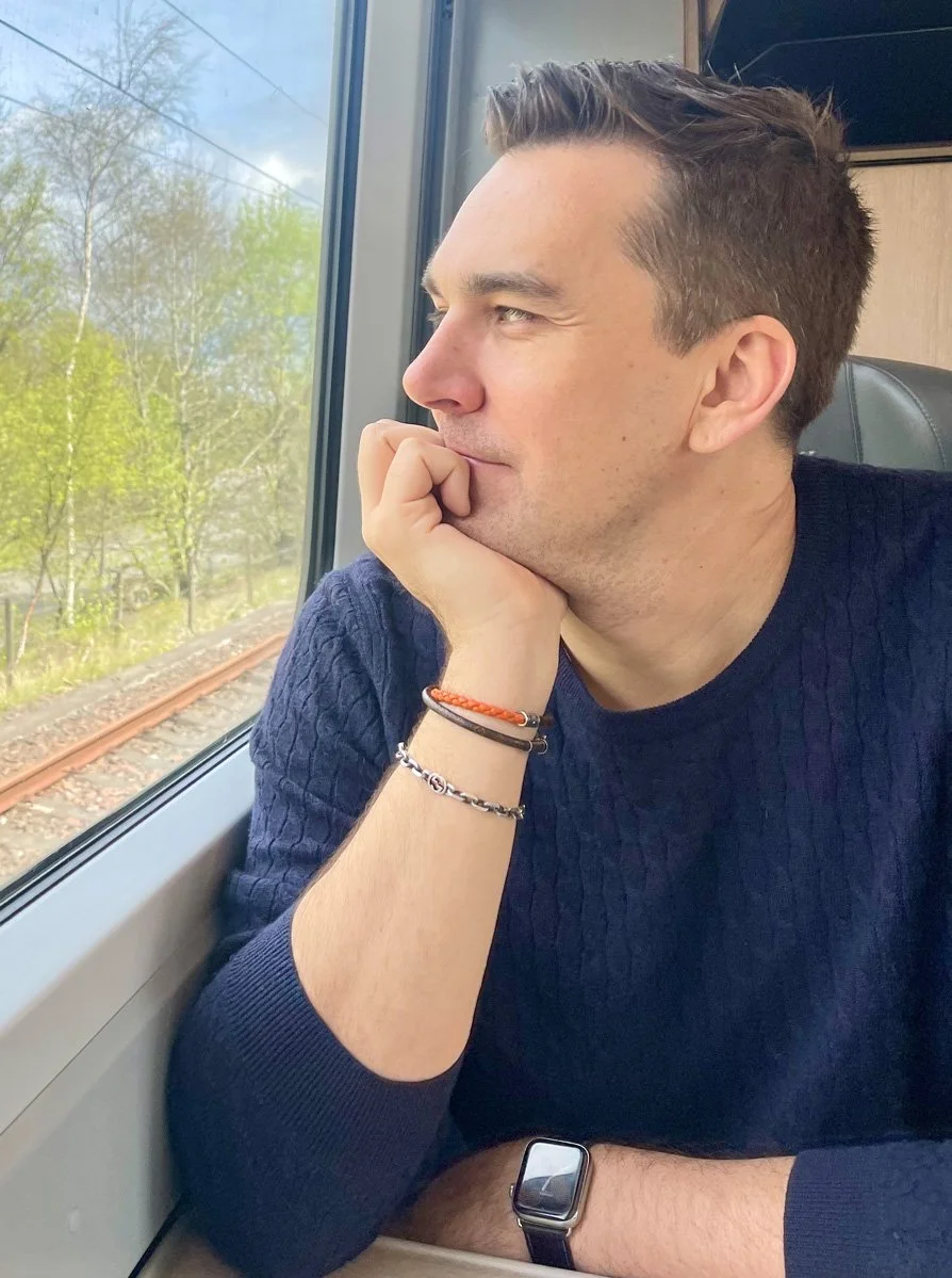 Brandon, sitting by a train window, looking thoughtfully outside.