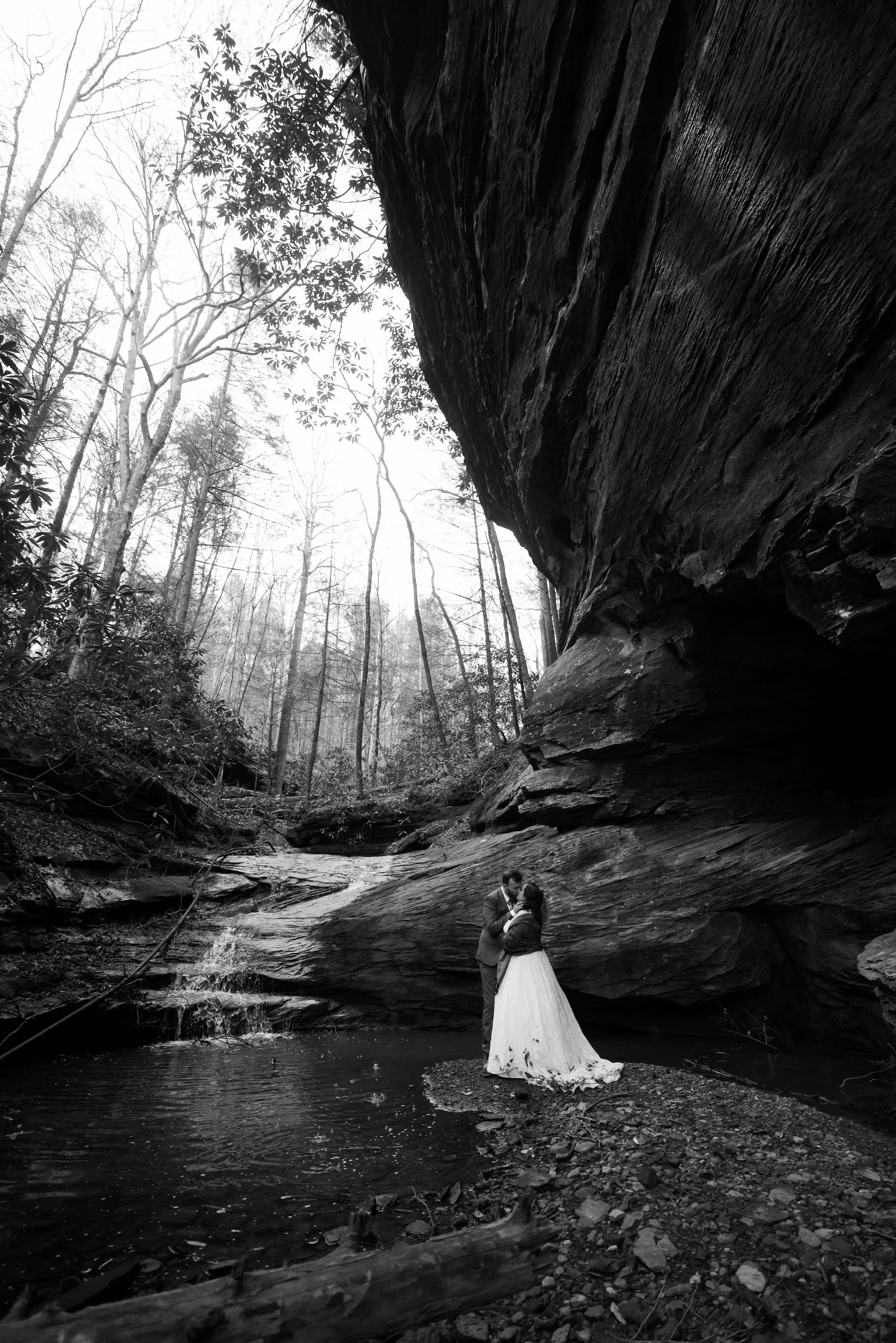  A photograph of a couple standing under a cliff in front of a waterfall during their luxury elopement planned by red river gorge weddings 
