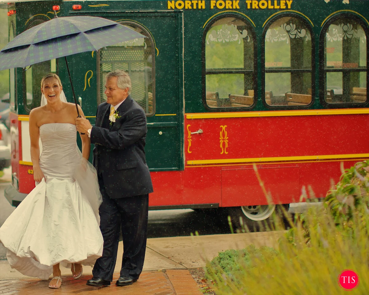 The father of the bride walks with her towards a church in The Hamptons in the pre-hurricane rain. Moment captured by Maring Visuals .