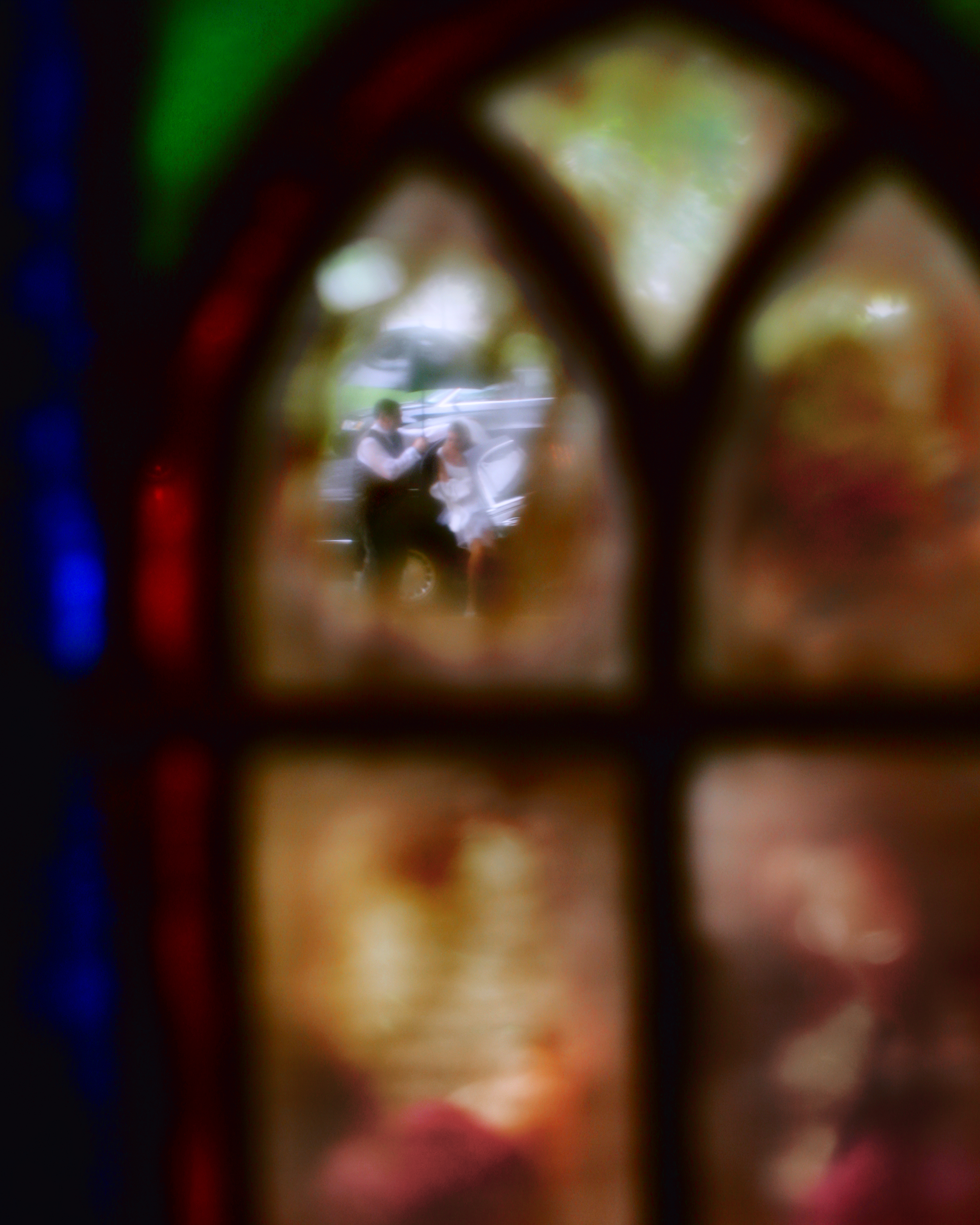 A bride rushes in from the limo to the church captured through a stained glass window in Connecticut. Moment captured by Maring Visuals