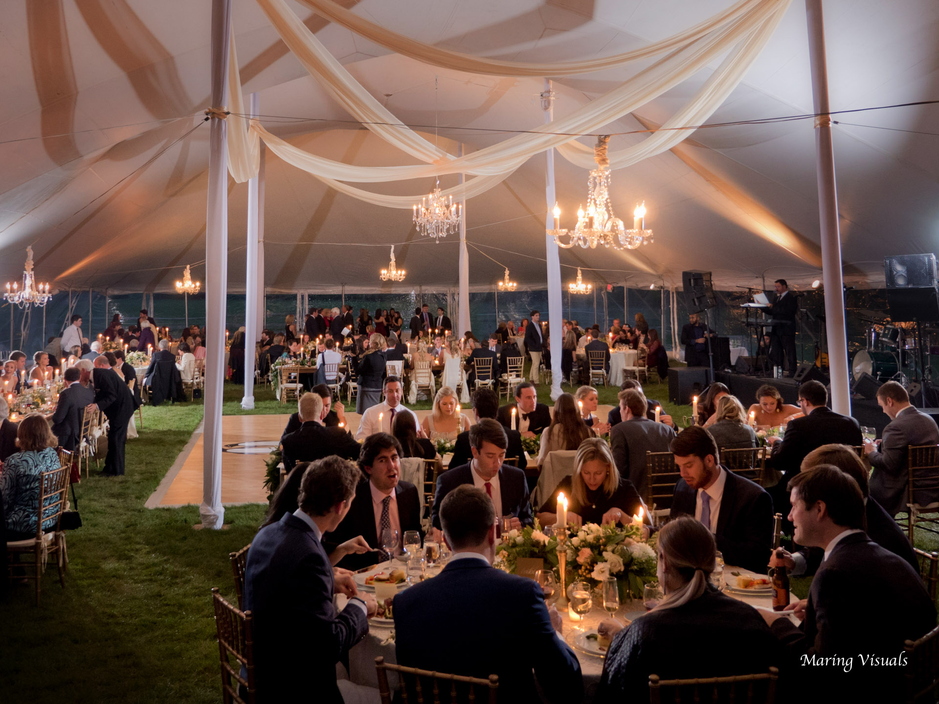 A mixture of round and long tables accented by chandeliers and candlelight have the tent a heartwarming atmosphere
