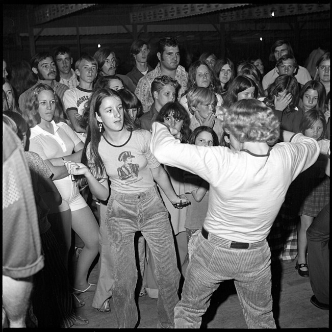 Note the expressions on the faces of the onlookers, who feel something other than swept up by the moves of the dancers in front of them. Their detachment and, in some cases, defiance opens up and deepens our sense of what is happening in the room. Photo by Bill Yates. Image via lenscratch.com .