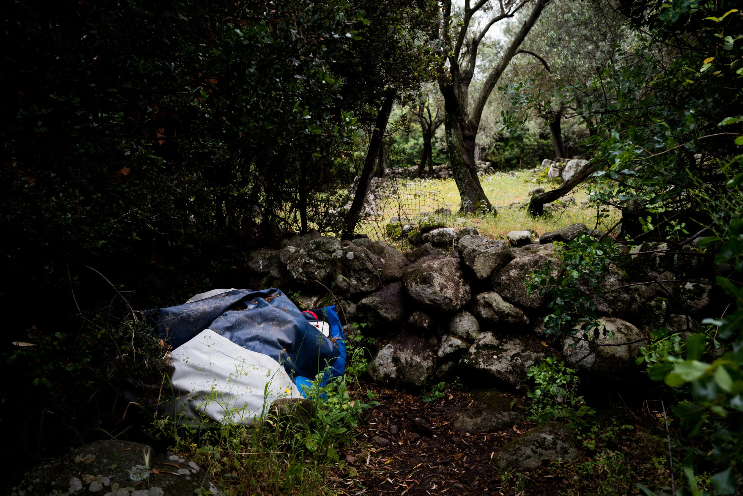 A rolled-up dinghy sits behind a grove of trees on a hiking trail near Skala Sikamineas.