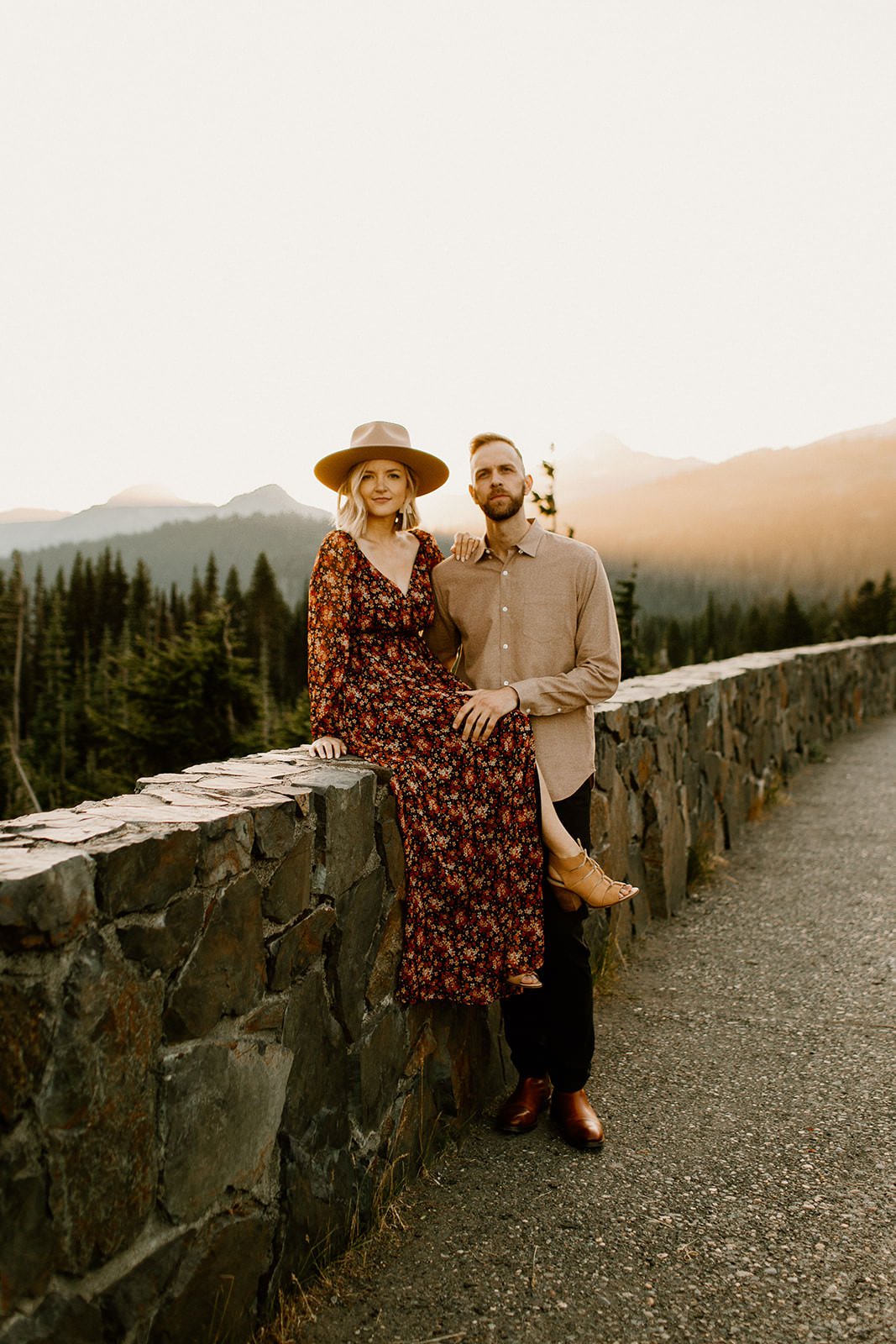 boho couple sitting on rock wall with mt. rainier in the background during their engagement session